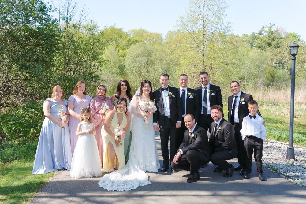 Wedding party in pastel dresses and dark suits posing outdoors on a spring day.