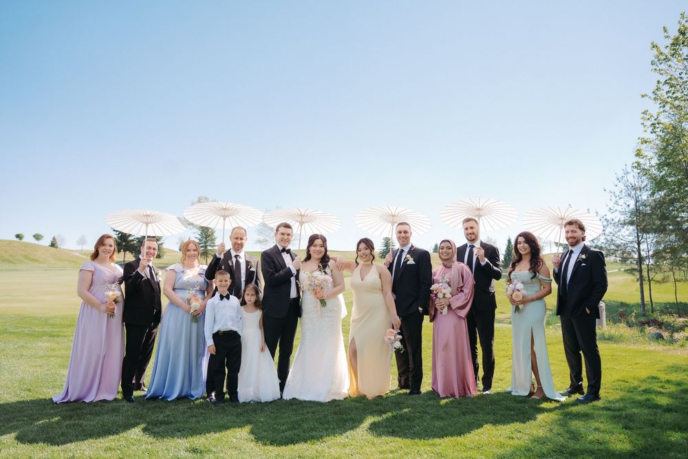 Wedding party in pastel dresses and dark suits pose together on sunny spring day.