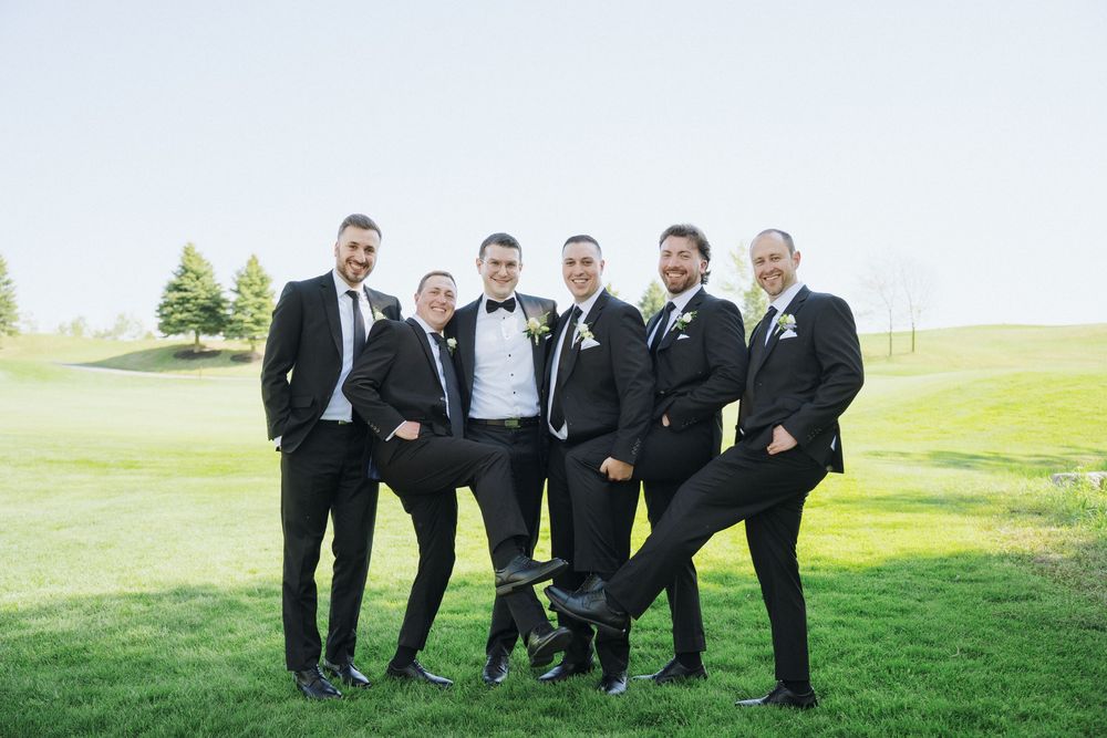 Wedding party in black suits smile and pose casually on golf course green.