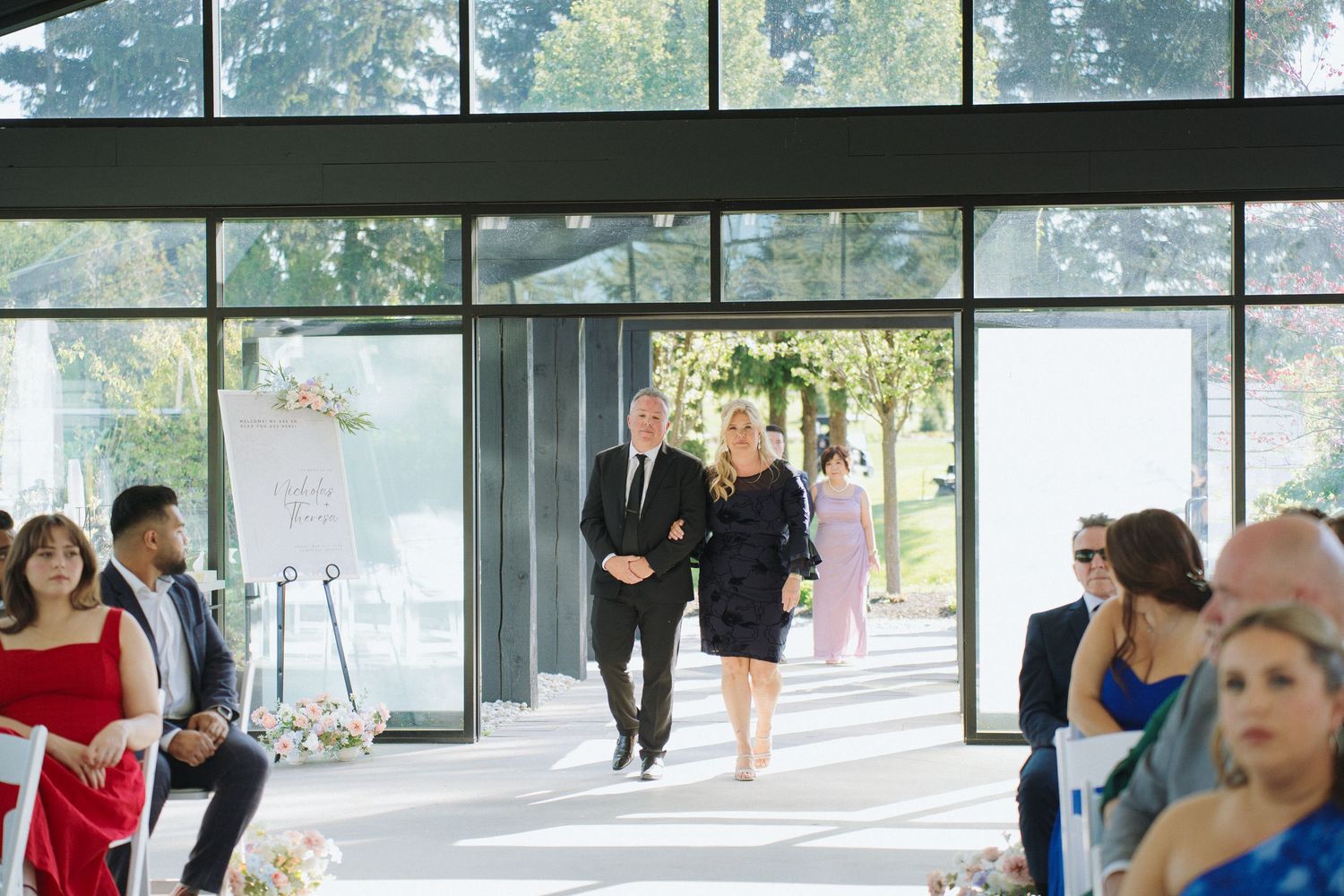 Wedding ceremony setup in bright venue with large windows and natural light streaming in.