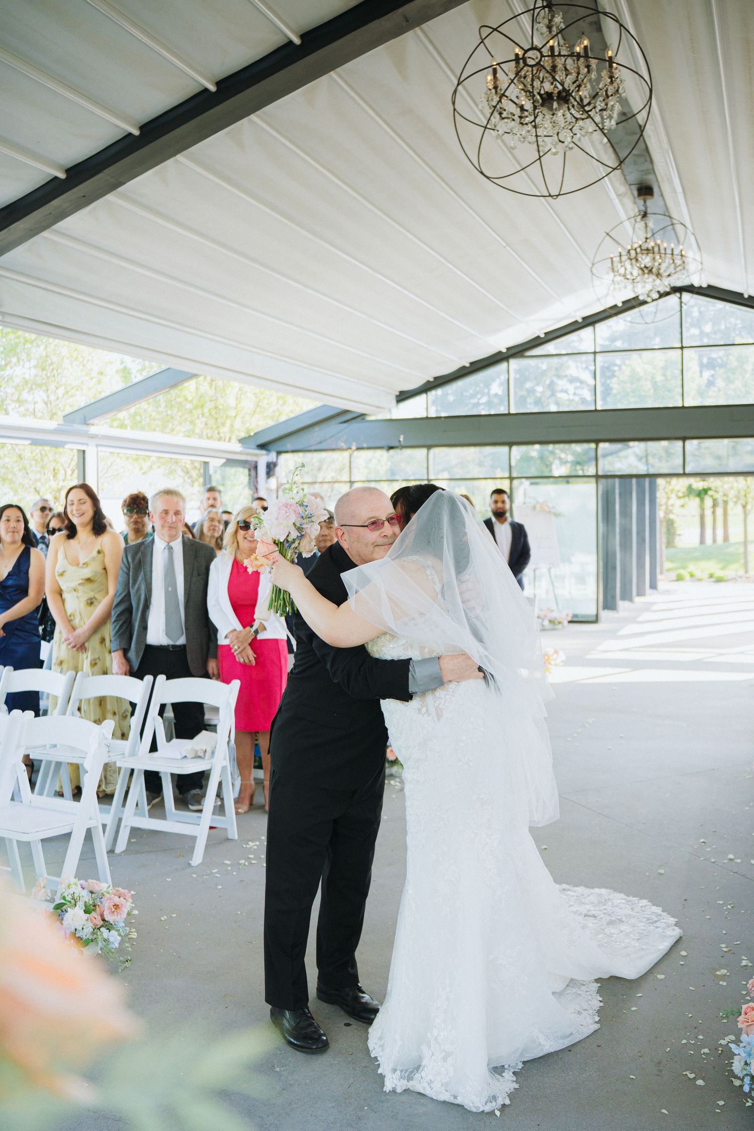 Wedding celebration in progress inside modern venue with white folding chairs and elegant lighting.