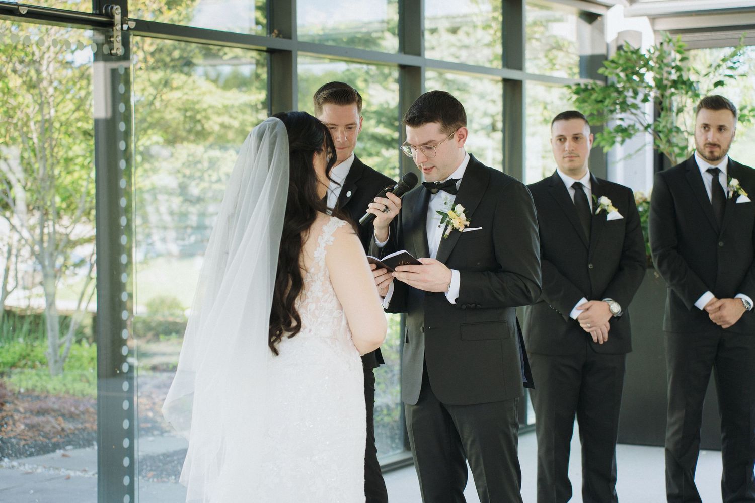 Couple exchanges rings during wedding ceremony with bridal party looking on.
