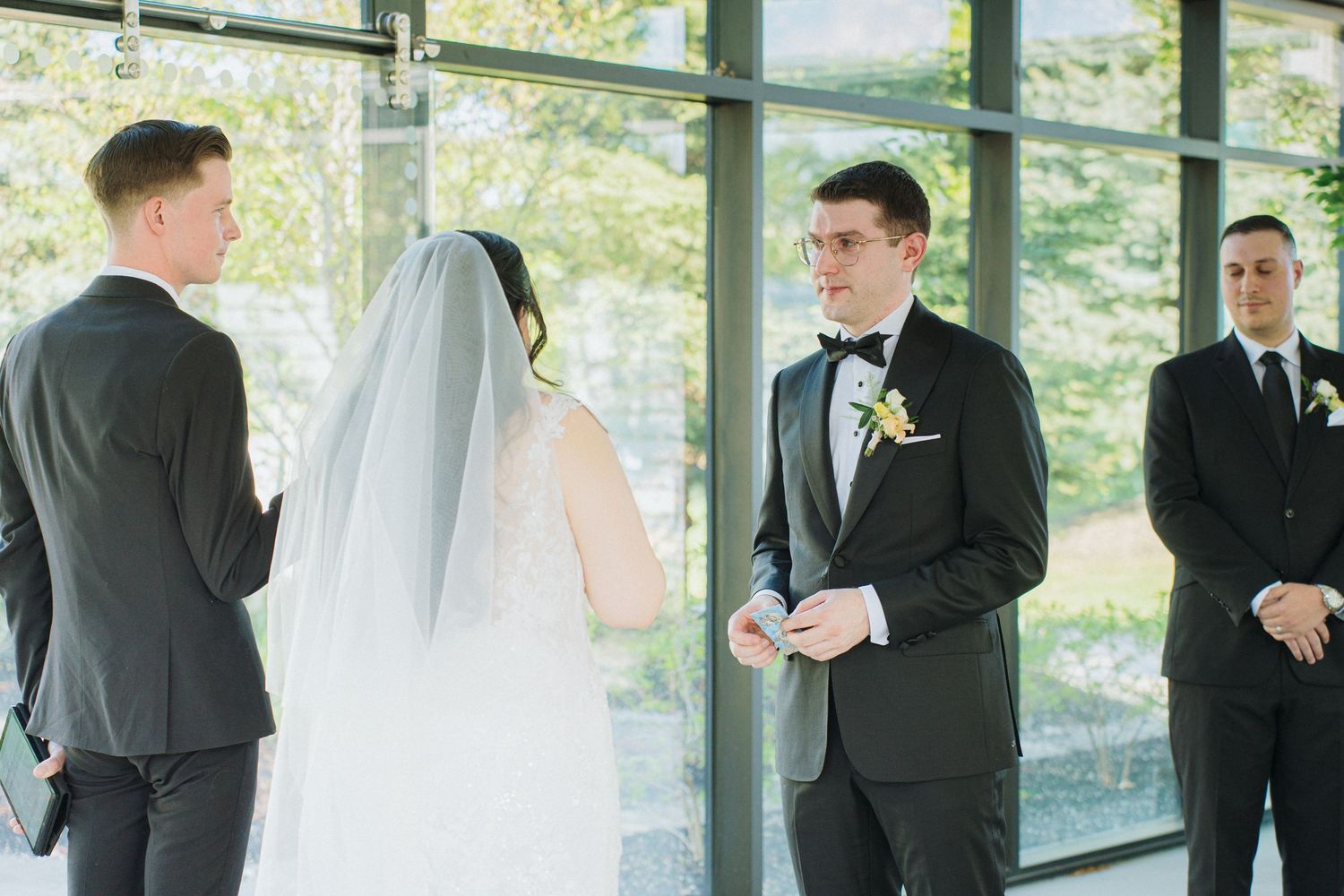 Officiant reads ceremony script to couple during wedding in glass-enclosed venue.