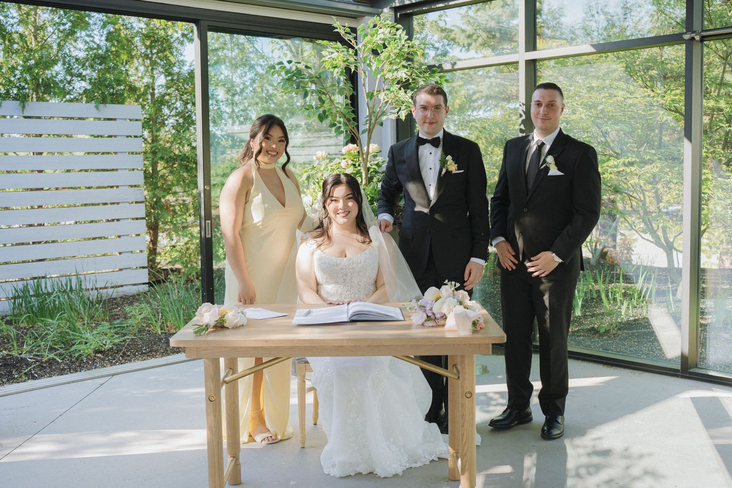 Wedding party gathers around signing table during marriage certificate ceremony.
