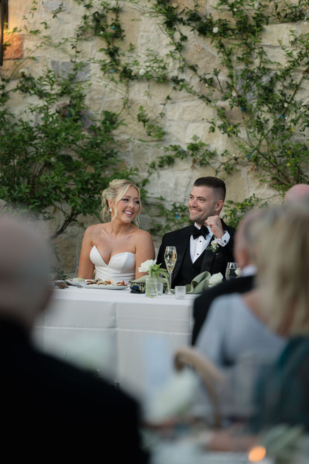 A wedding reception at an elegant outdoor venue with ivy-covered walls and a formal table setting.