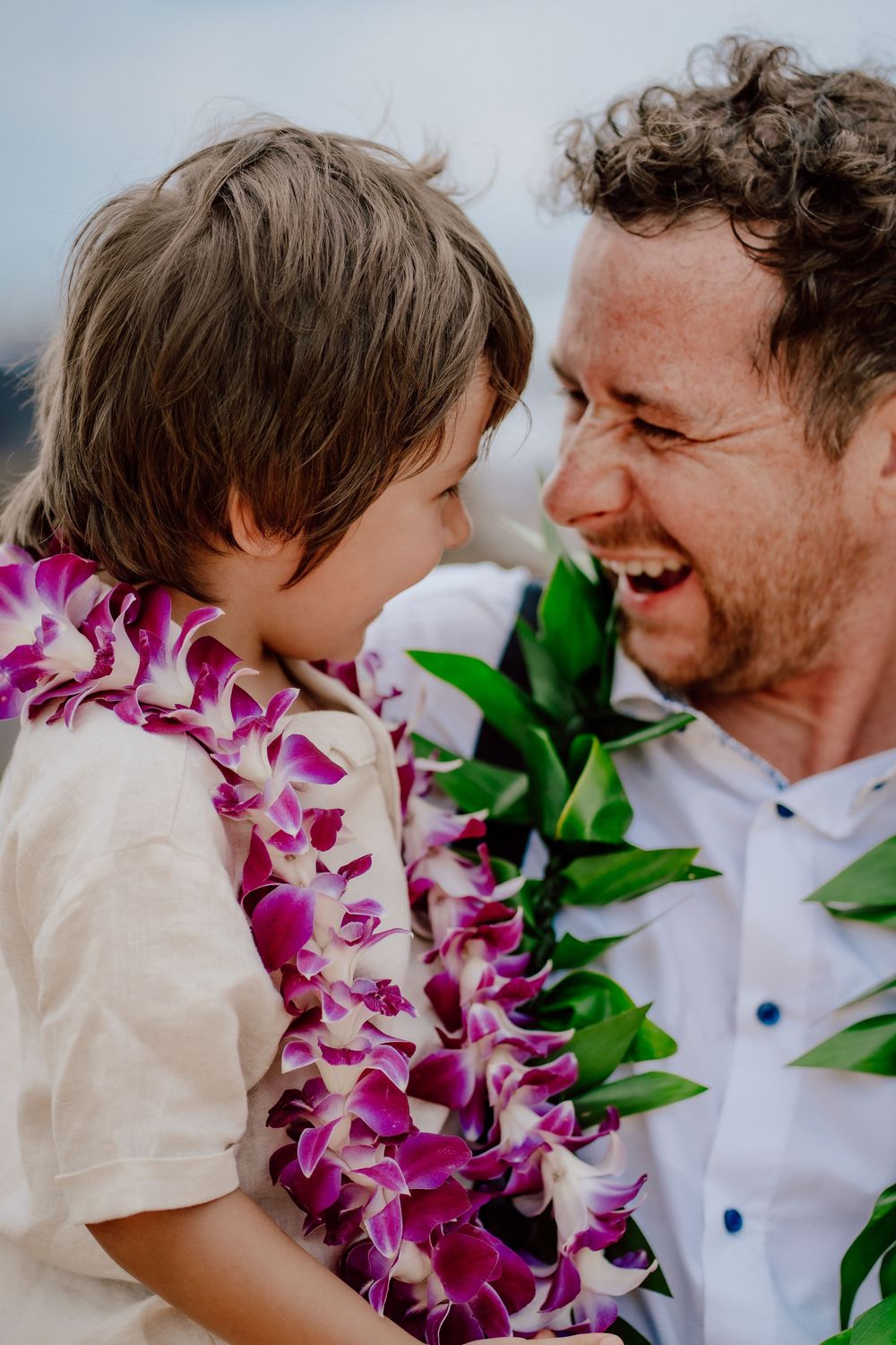 A joyful moment shared between two people wearing traditional Hawaiian leis with vibrant purple orchids at sunset.