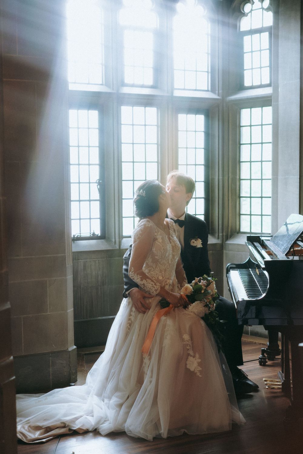 Elegant wedding party poses in a sunlit room with classic wood paneling and large windows.