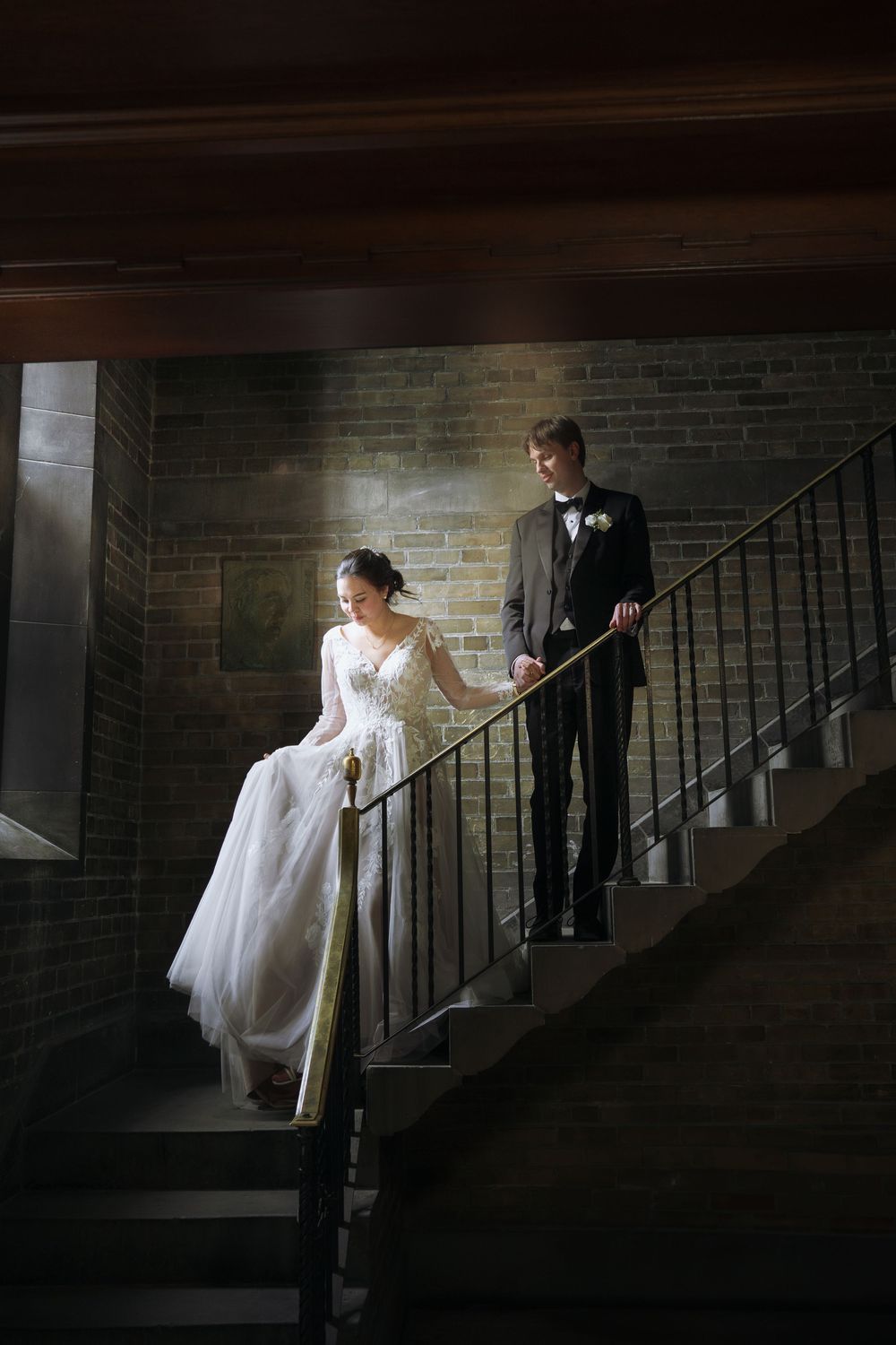 Dramatic staircase and brick wall create moody wedding photo composition.