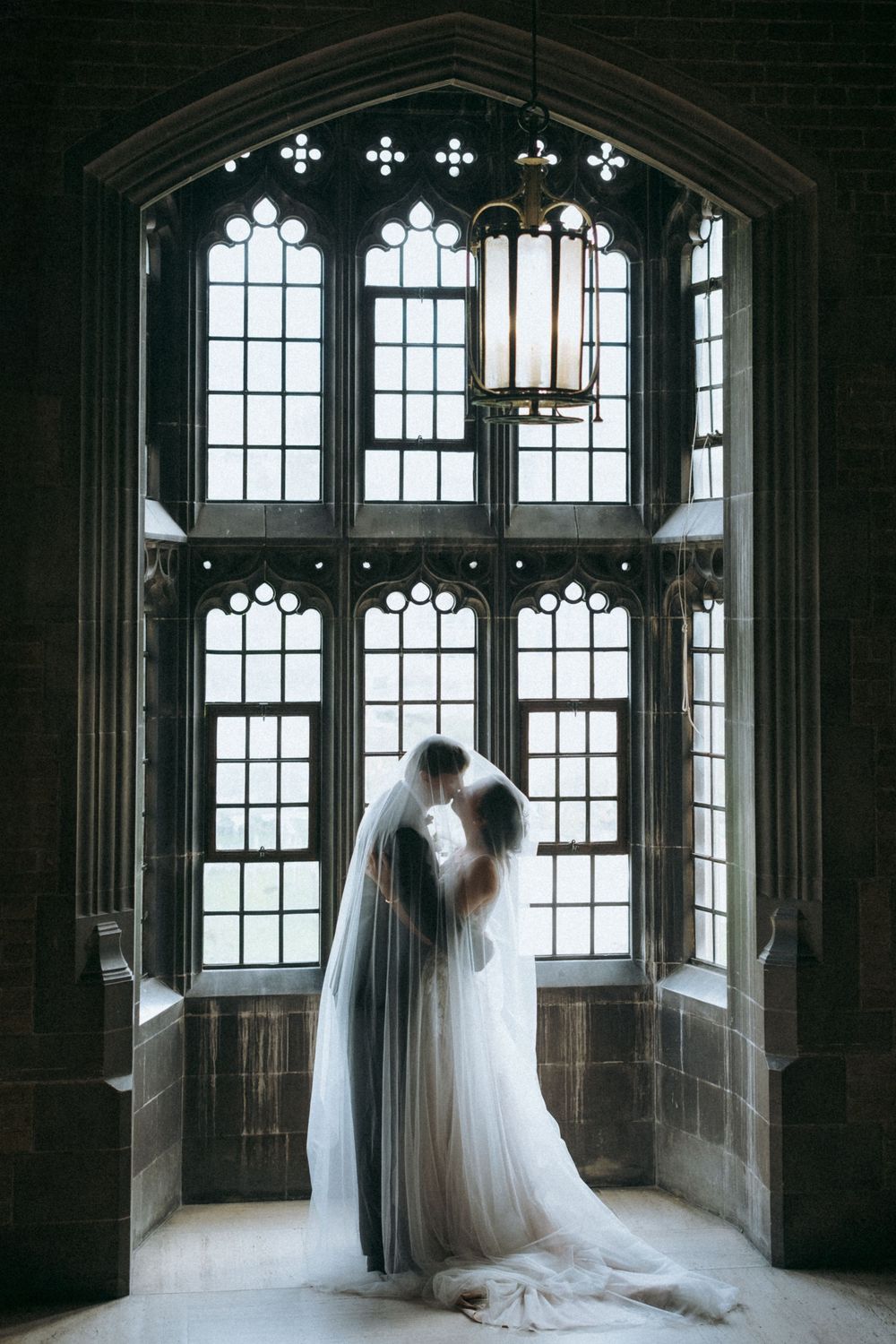Silhouetted couple embraces by dramatic gothic windows in historic building.