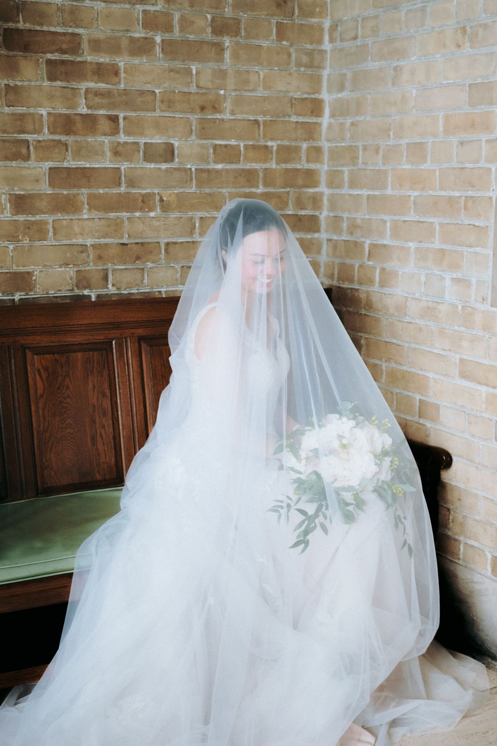 Flowing white wedding dress and veil detail against exposed brick wall.