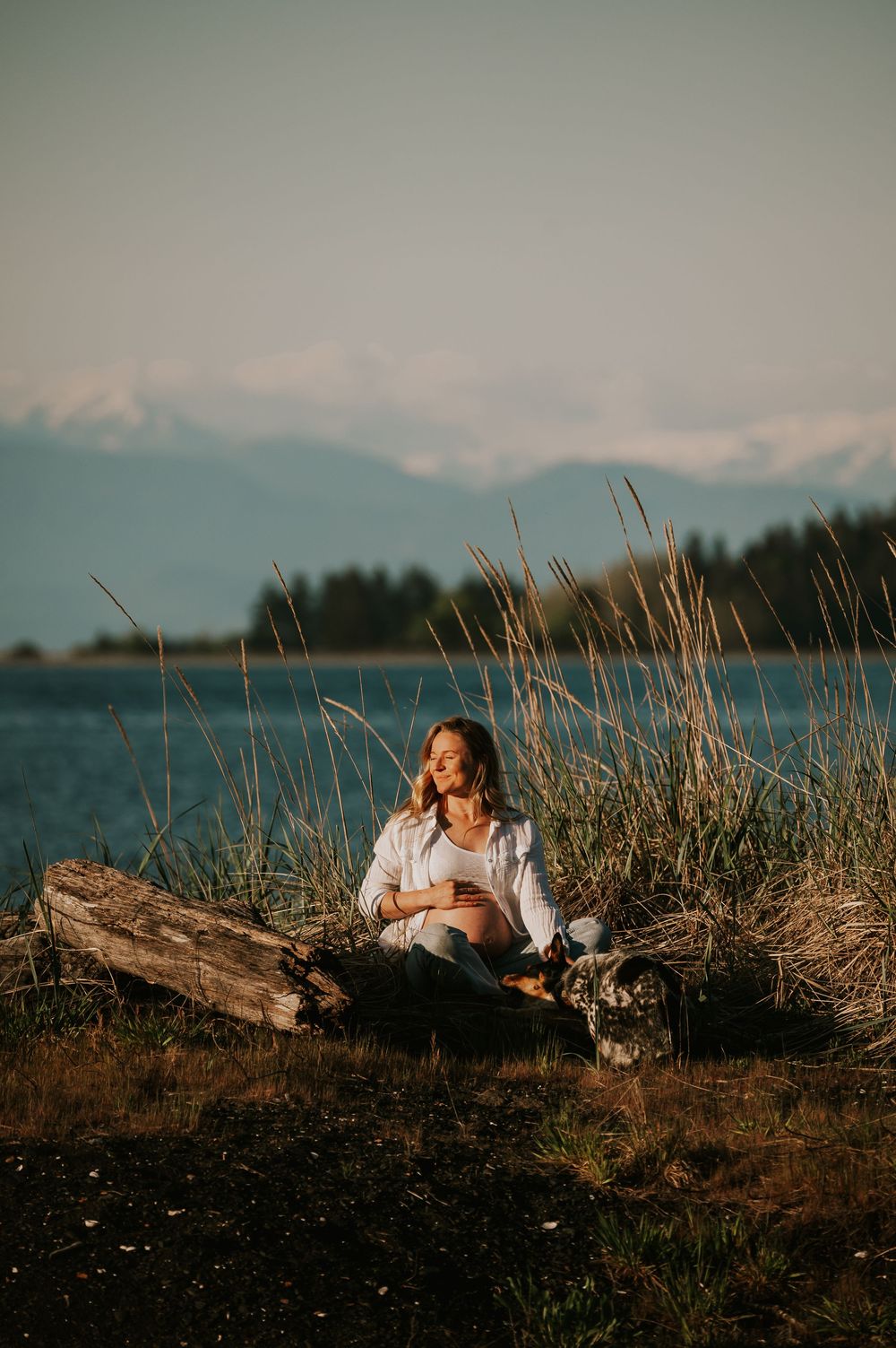 Maternity photoshoot in Comox Valley on Vancouver island woman embracing pregnant belly sitting in sun outdoor natural light photographer