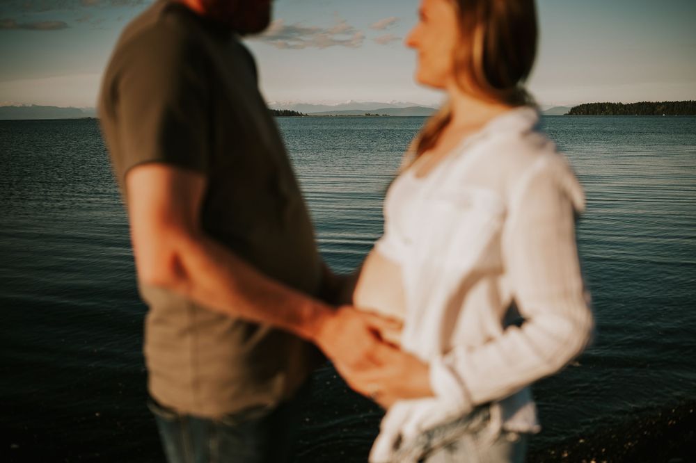 Maternity photoshoot by ocean on black sand beach Vancouver island ocean portrait through couples hands outdoor natural light photographer