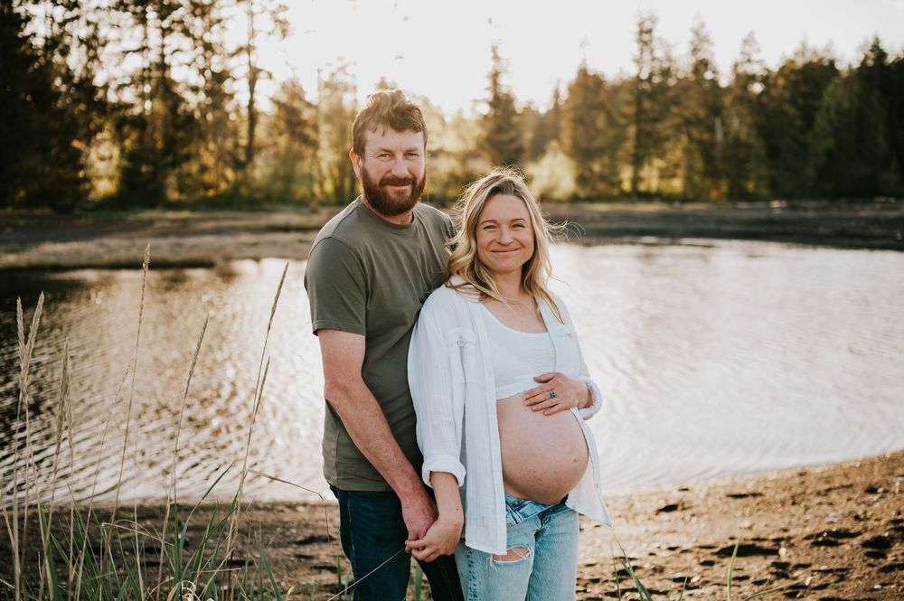 Maternity portrait of couple smiling at camera by ocean on black sand beach Vancouver island outdoor natural light photographer