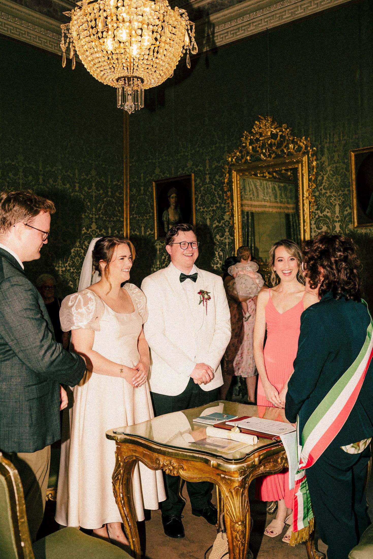 Wedding ceremony in ornate room with crystal chandelier and vintage decor.