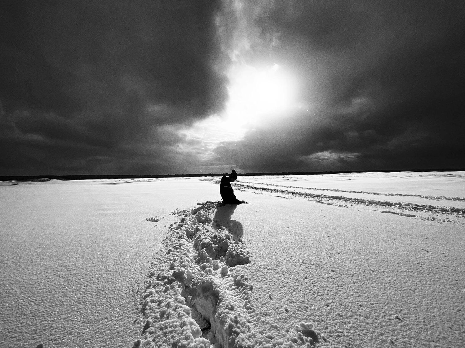 Osoba klęcząca samotnie na ośnieżonym pustkowiu w czarno-białym krajobrazie – fotografia artystyczna autorstwa Anety Ludwig.