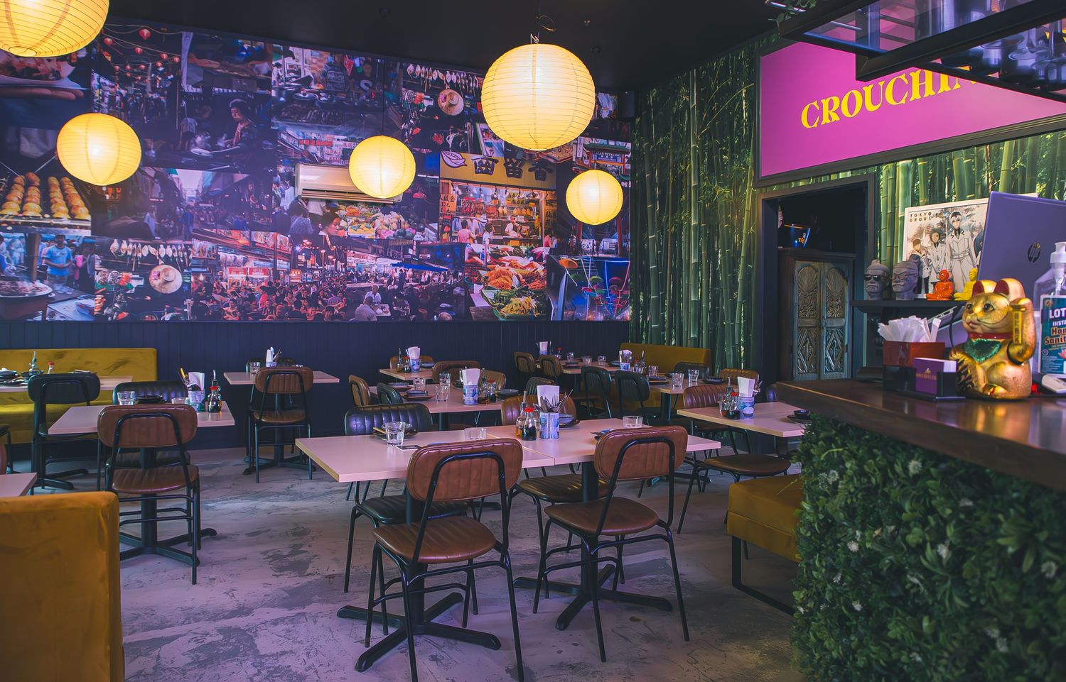 Modern restaurant interior with glowing orange lanterns, purple wall art, and wooden tables and chairs in an ambient setting.