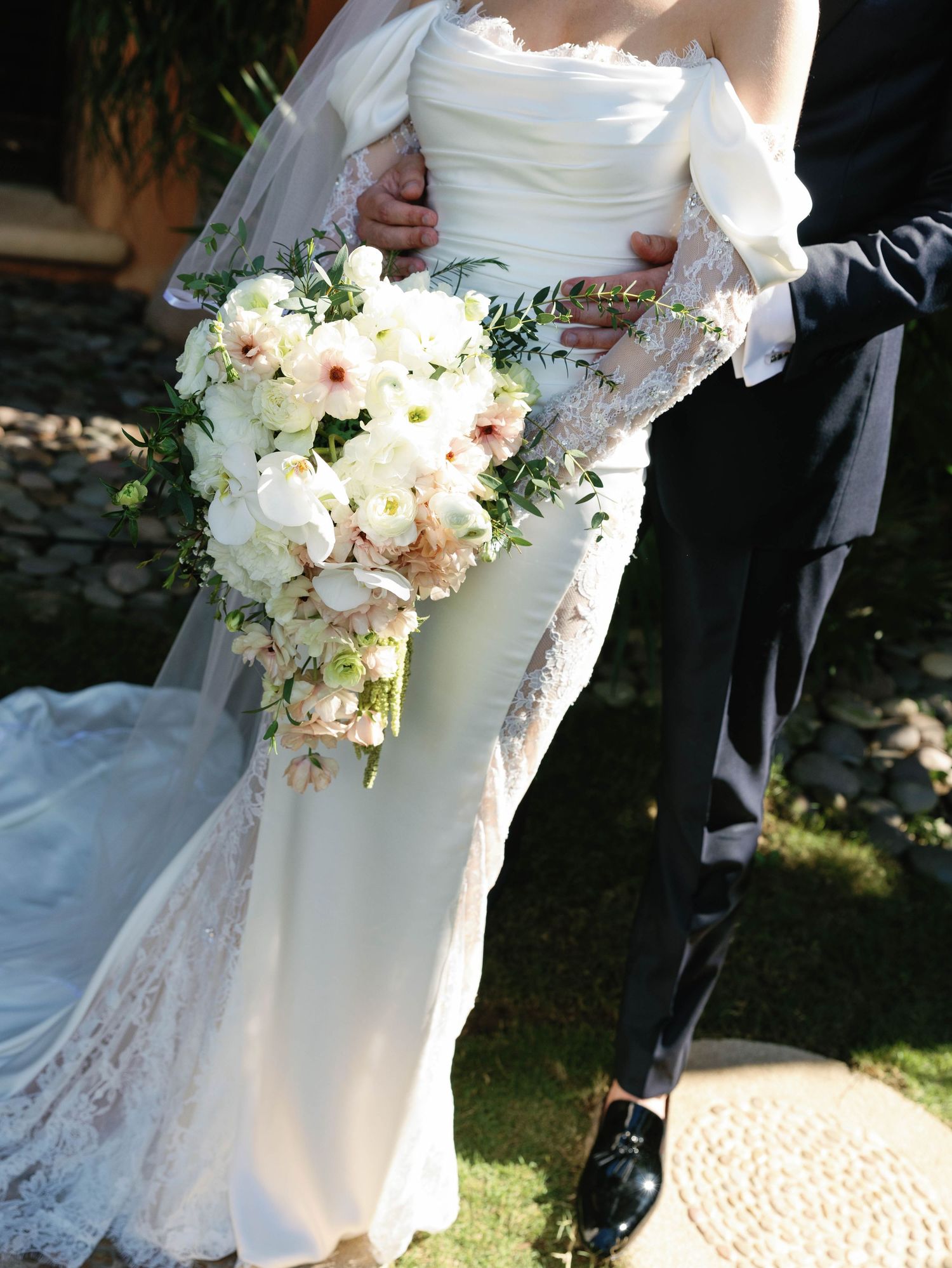 Close-up of cascading white and blush bridal bouquet against lace wedding gown.