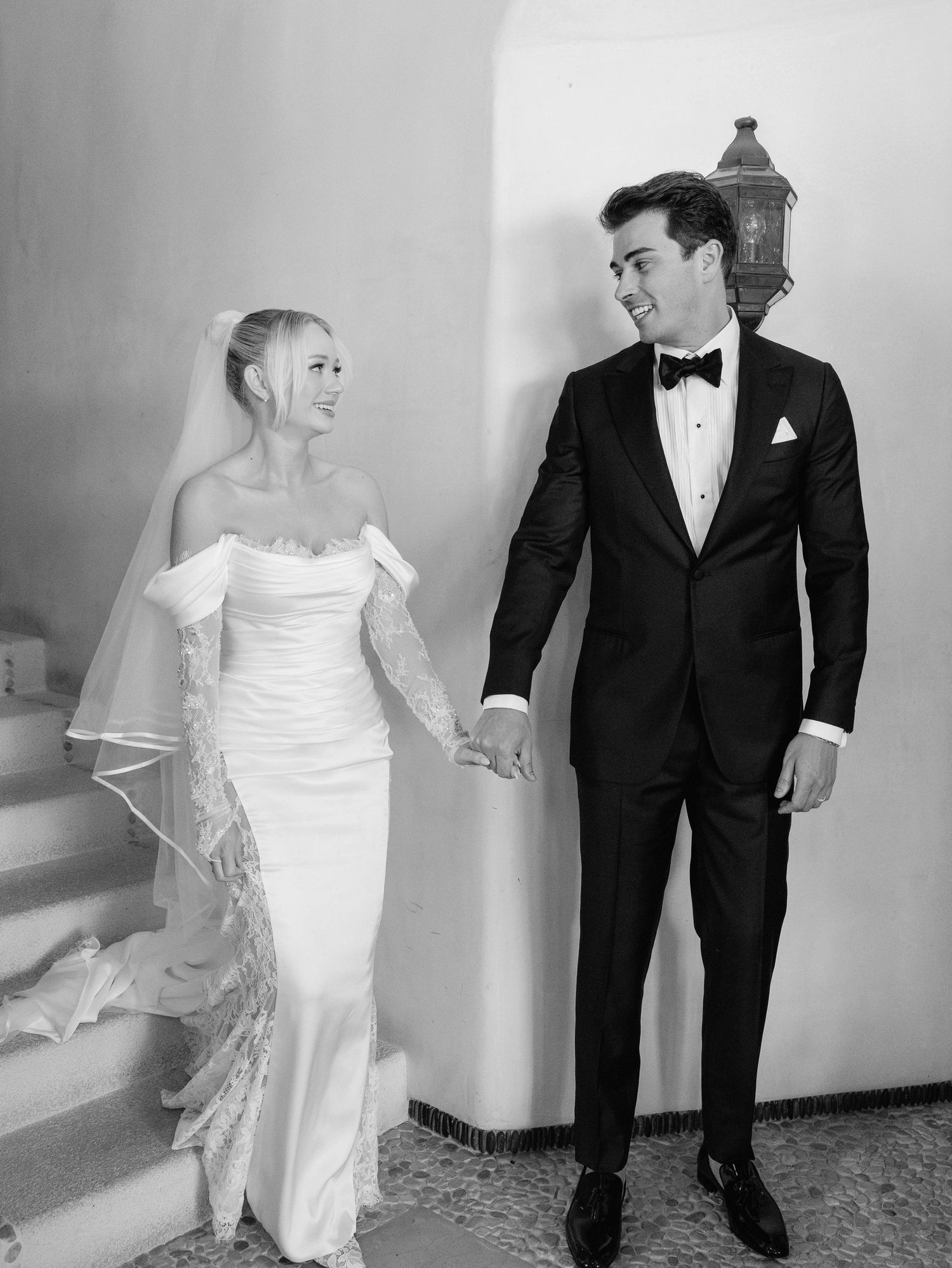 Elegant couple in wedding attire share a loving glance on stone staircase beneath vintage lantern.
