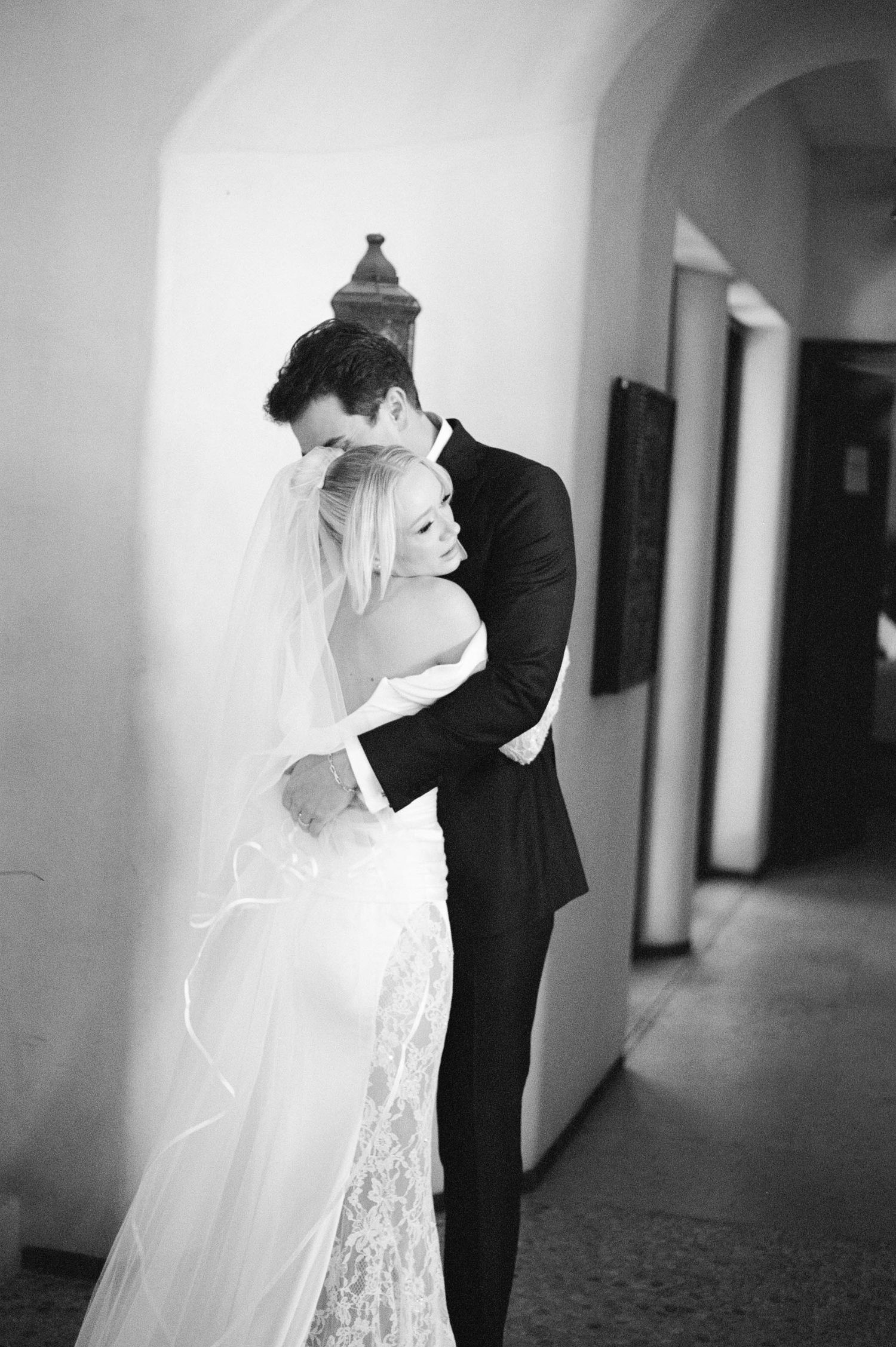 Romantic black and white portrait captures intimate embrace in arched hallway.