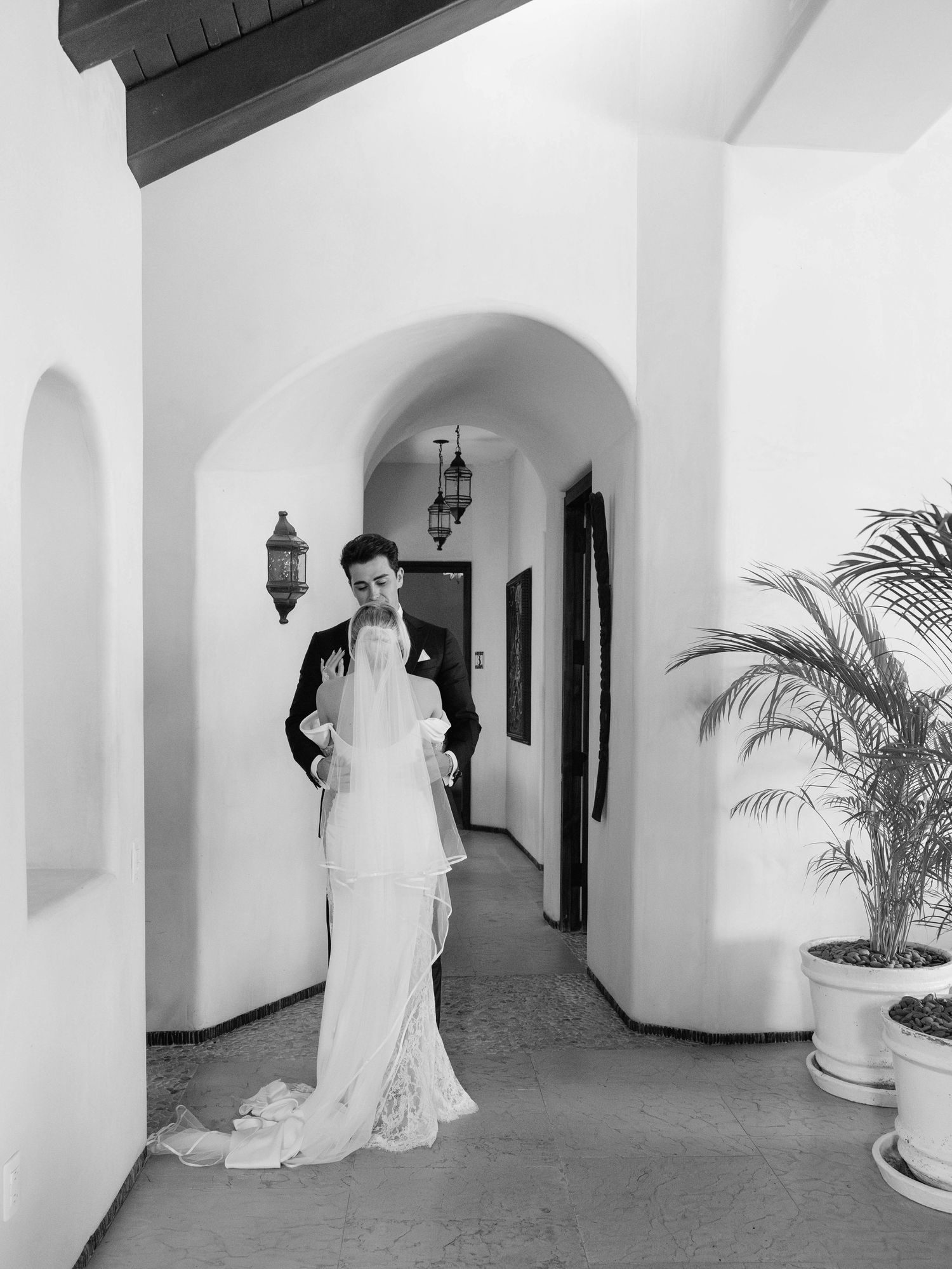 Elegant wedding couple poses in Mediterranean-style hallway with arched details and potted palms.