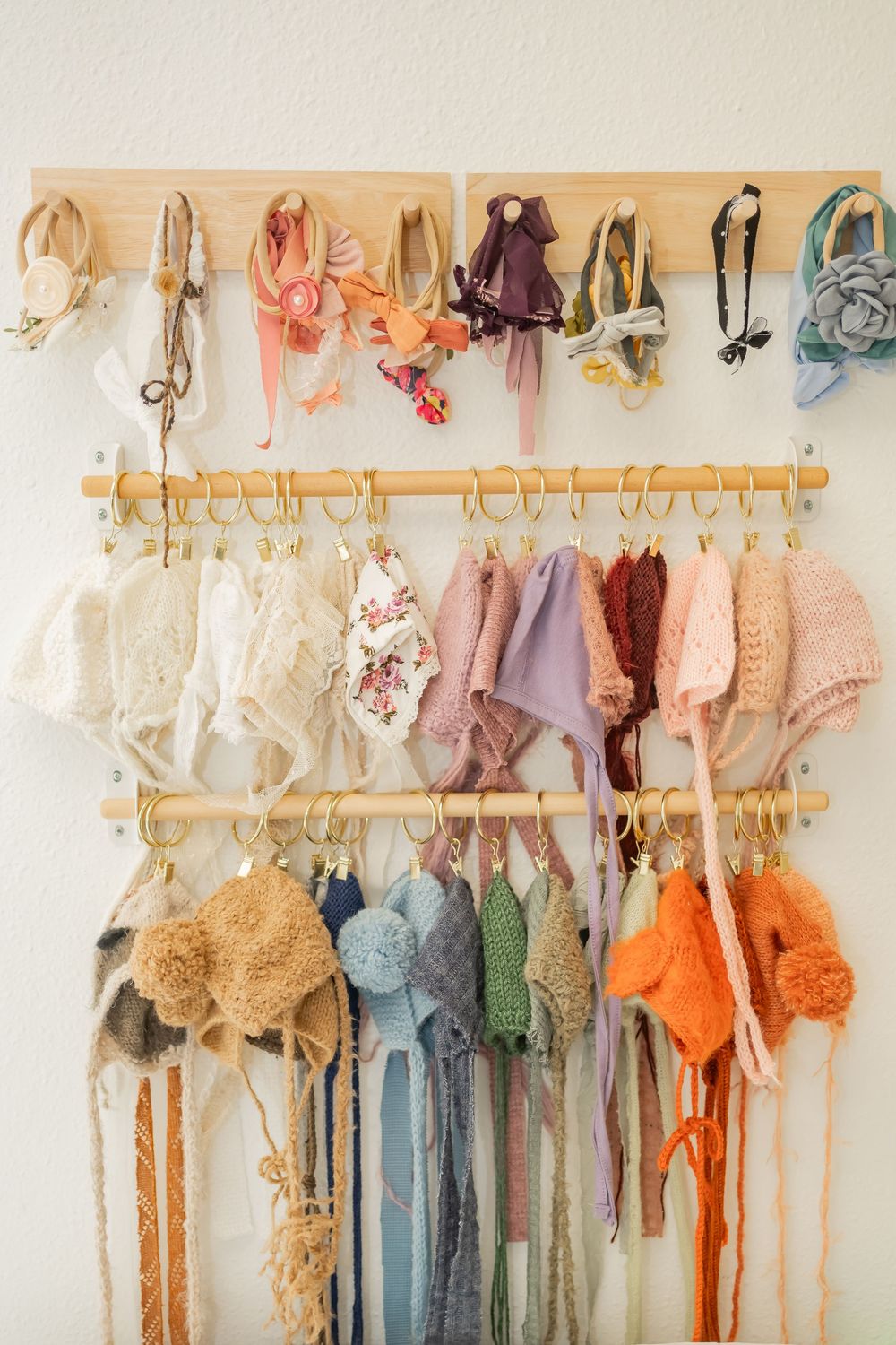 Organized display of pastel baby clothing and accessories hanging neatly on wooden rods against a cream colored wall.