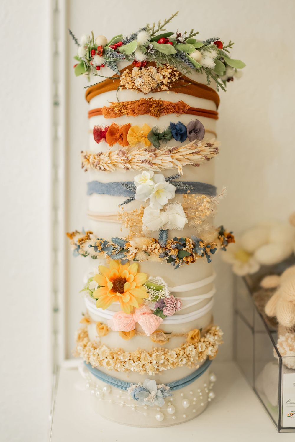 Elegant white tiered wedding cake decorated with blue ribbons, delicate flowers, and pearl embellishments against neutral background.