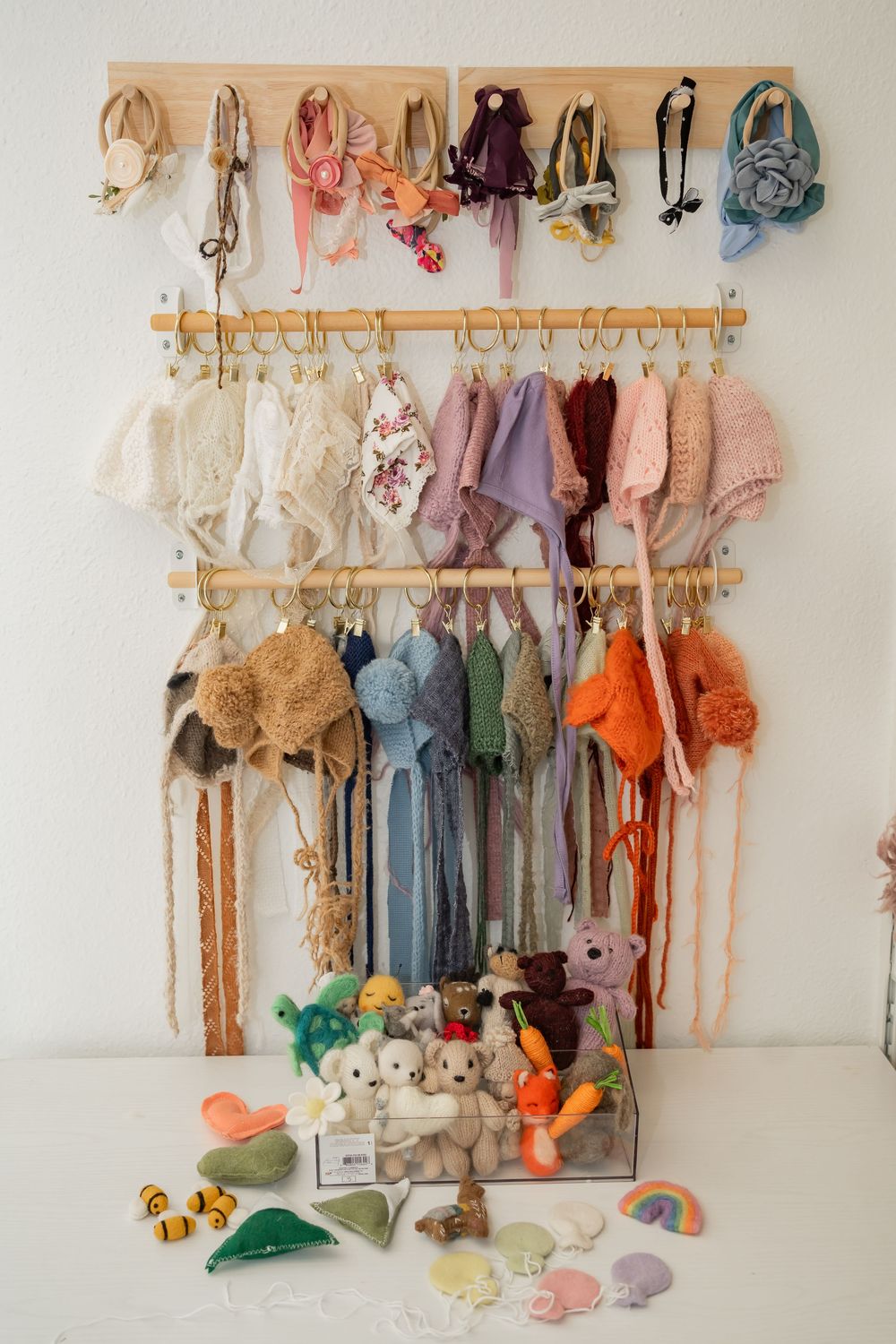Organized display of colorful plush toys, dolls, and stuffed animals hanging on three-tiered wall mounted hooks with toys below.