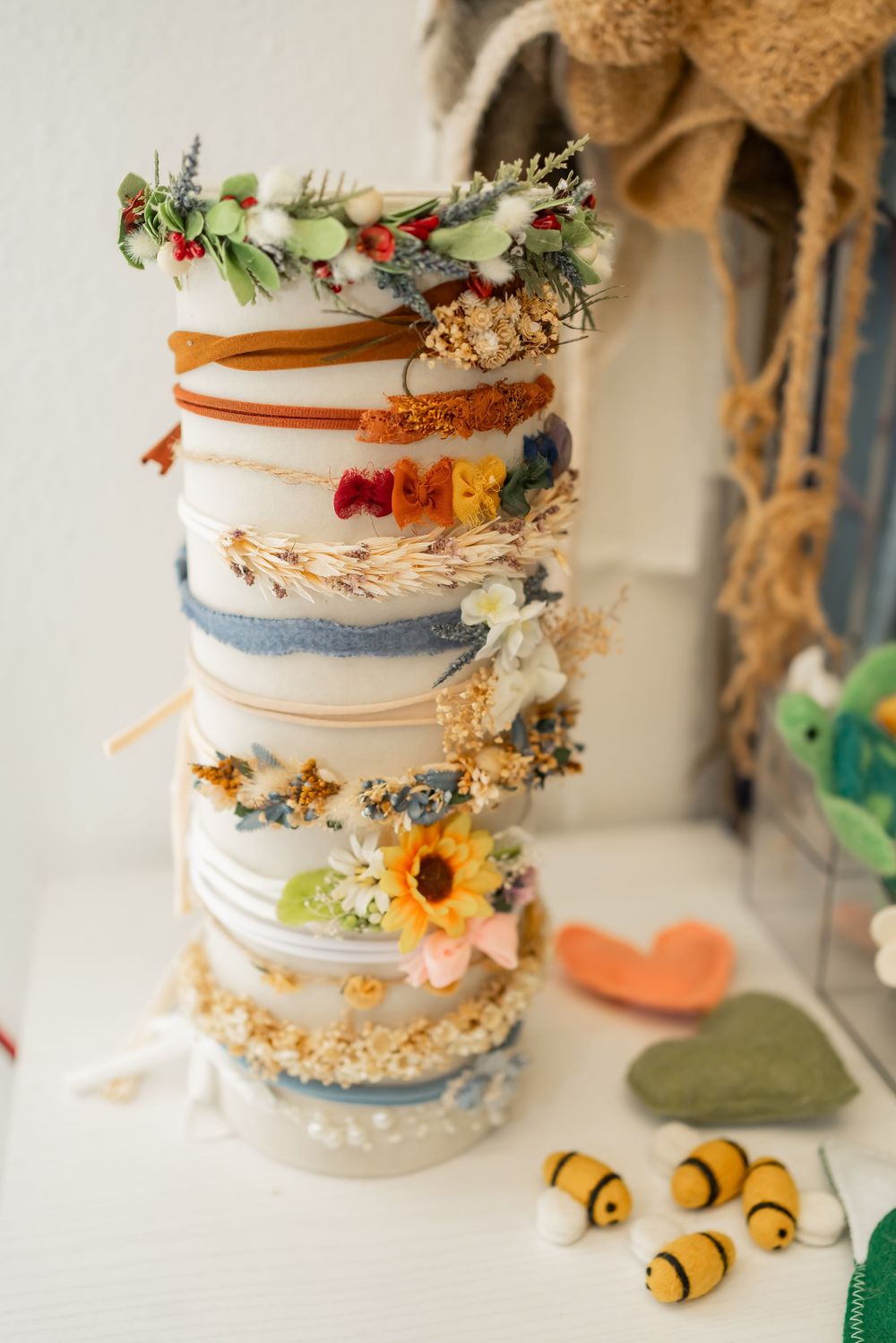 A tiered white wedding cake decorated with dried flowers, blue accents, and whimsical bumblebee decorations on the table.