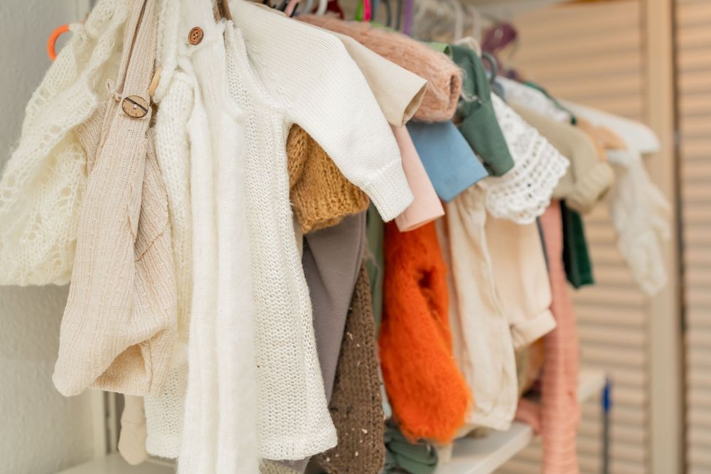Delicate children's clothing hanging on hangers with white lace dresses and colorful garments in soft natural light.