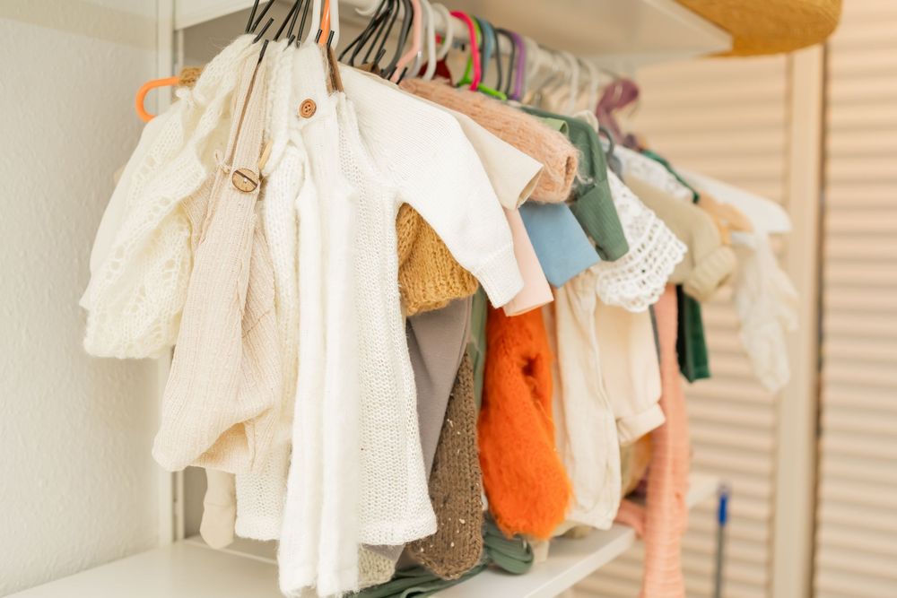 White baby clothes and infant garments hanging on hangers in a nursery closet or clothing rack.