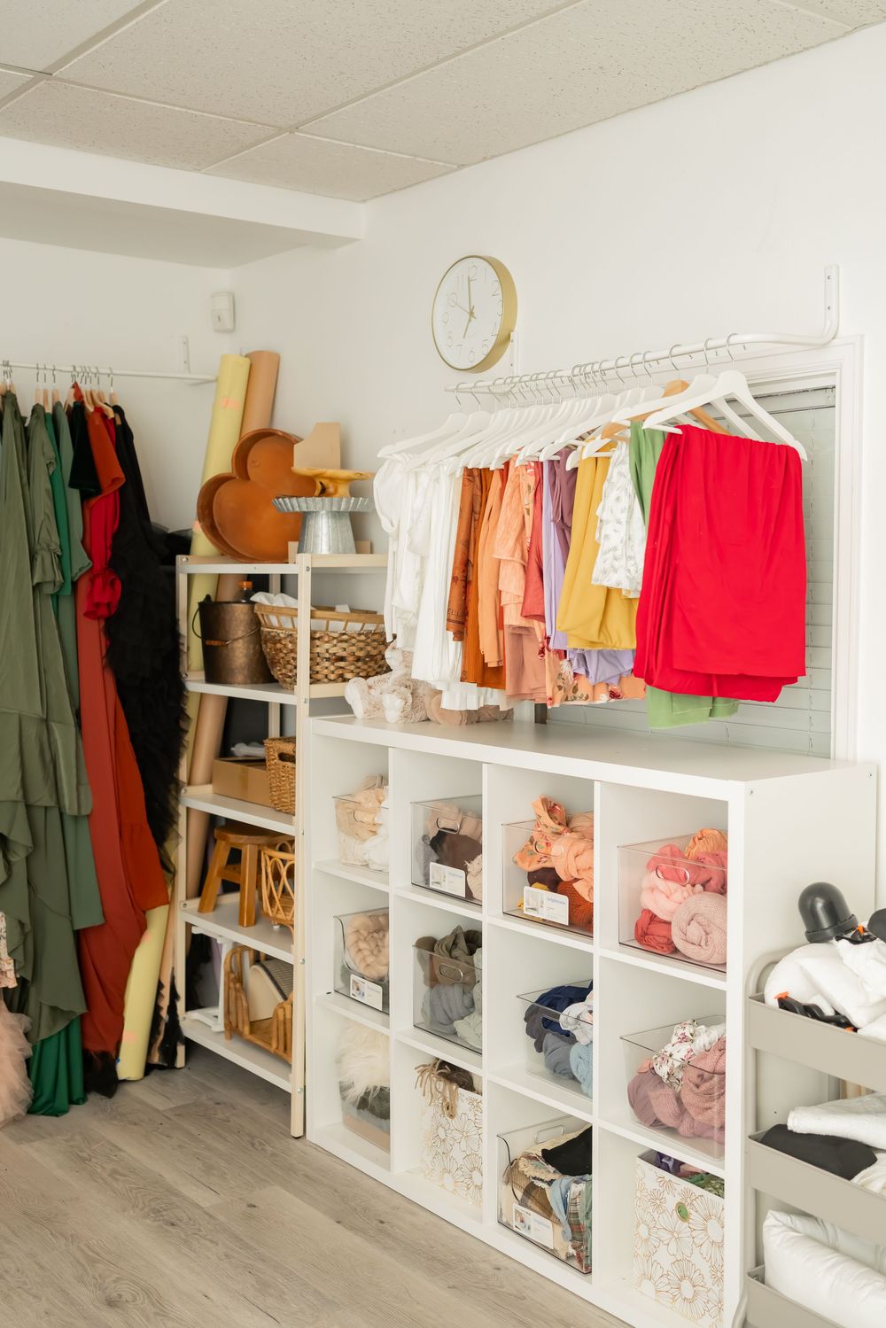 Organized walk-in closet with white shelving units displaying colorful clothing, shoes, and accessories on multiple levels.