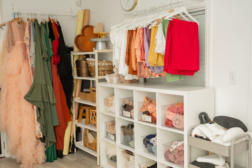 A clean, organized closet with white cubby shelves storing folded clothes and hanging garments in soft pastel colors.