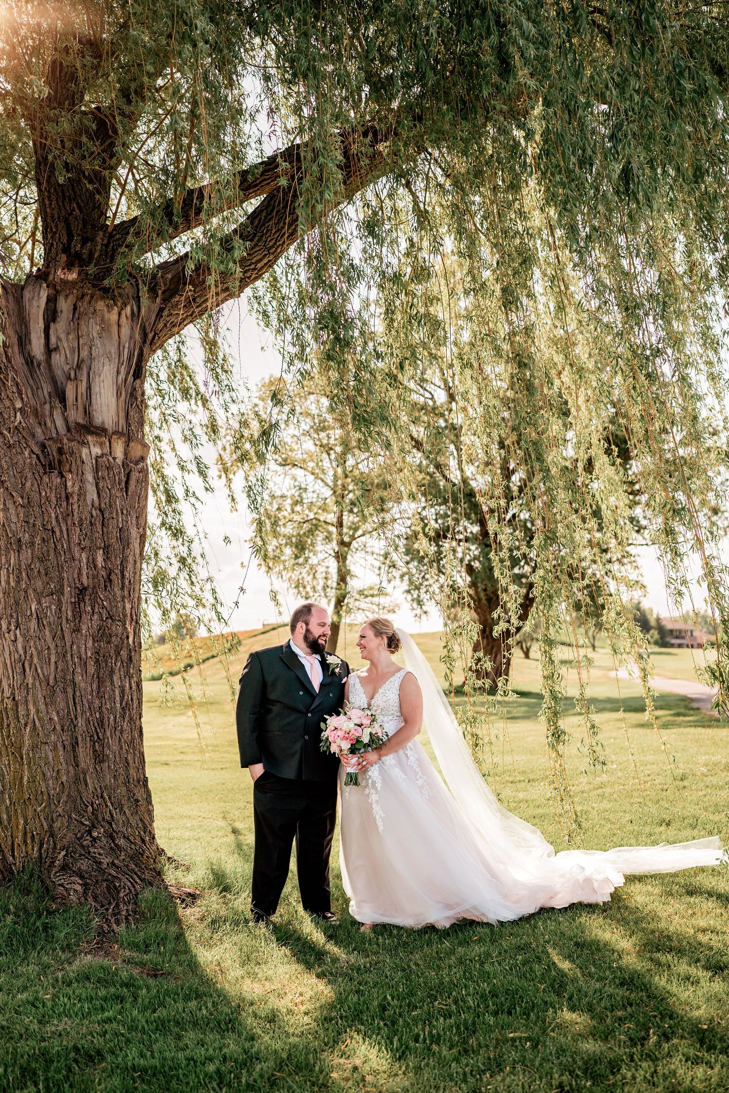 Romantic wedding portrait under a weeping willow tree on a sunny day.