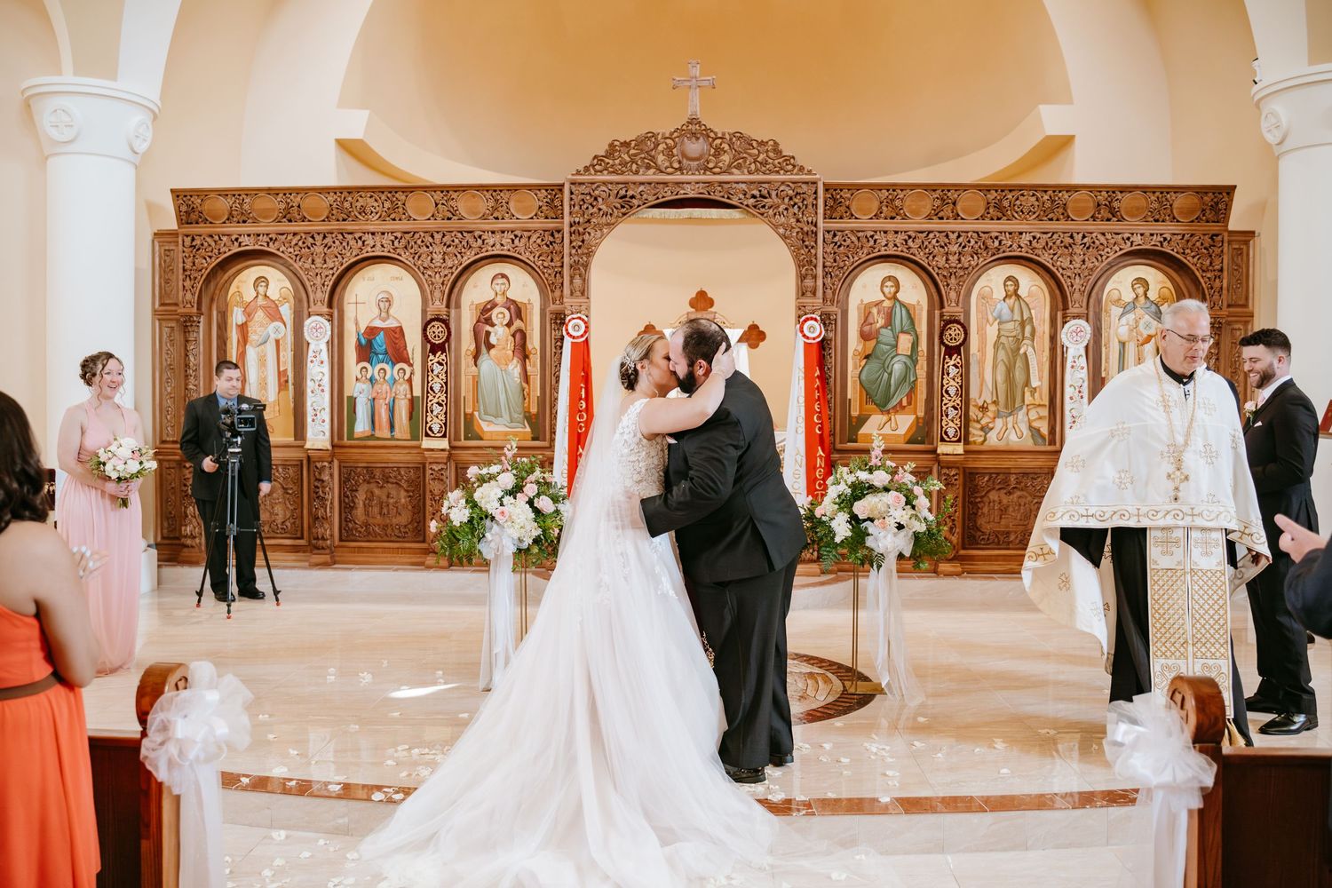 Traditional Orthodox church ceremony with ornate iconostasis and floral arrangements at the altar.
