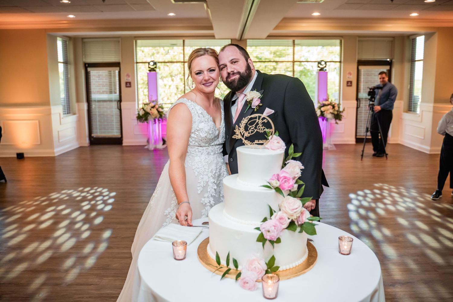 Elegant white wedding cake with pink floral decorations on display at a reception.