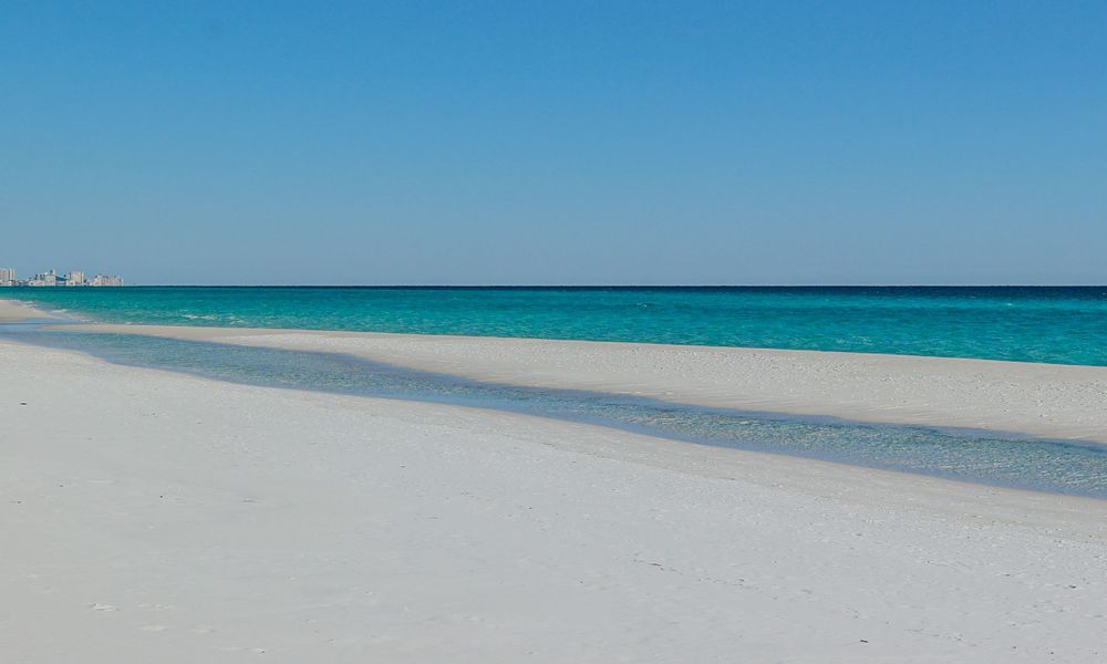 Pristine white sand beach meets turquoise waters under clear blue skies along a tranquil tropical coastline.