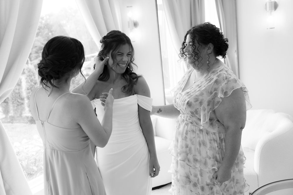 Three women share an intimate moment while getting ready in a light-filled room on wedding day.