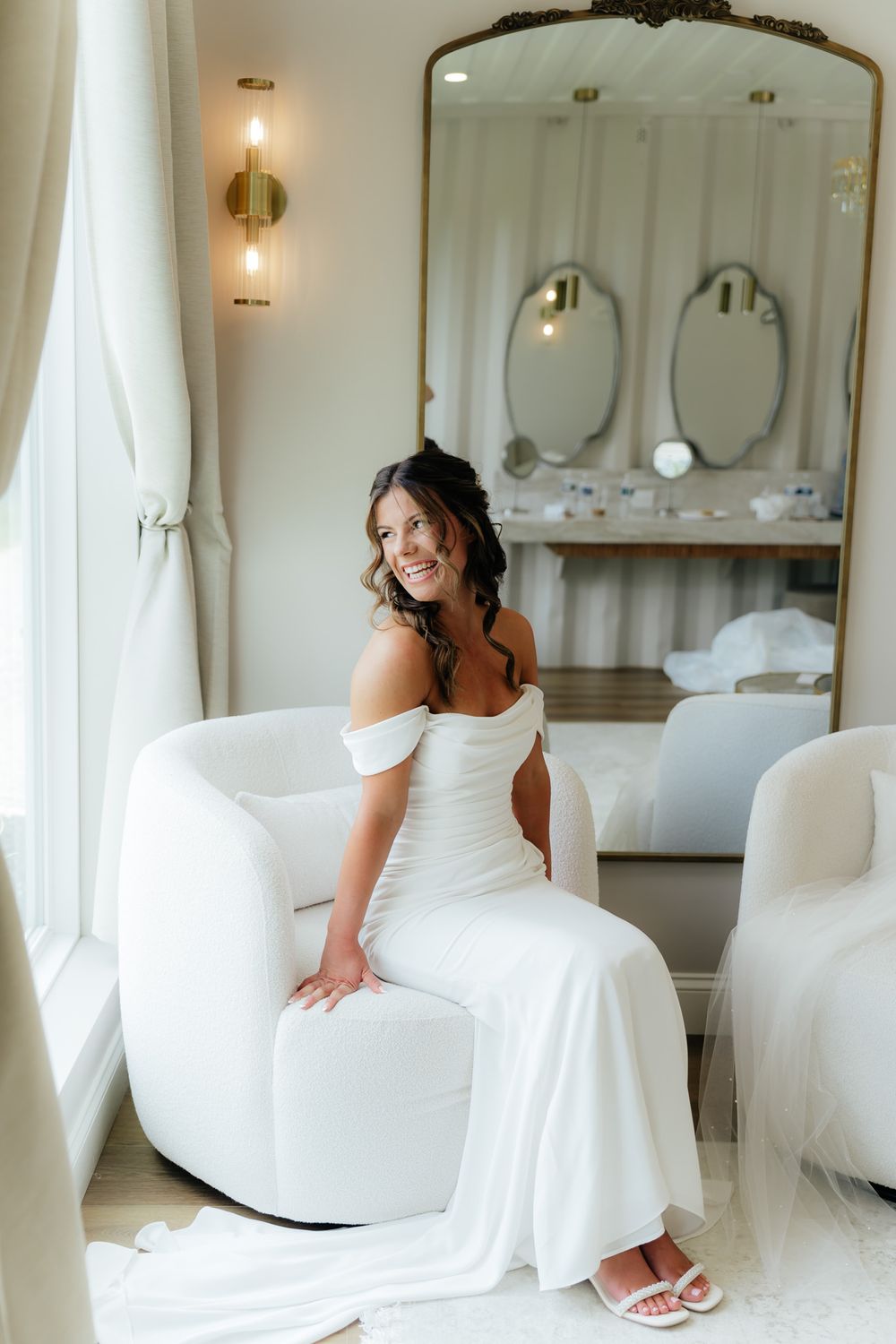Elegant bridal suite with white modern furniture, vintage mirror, and floor-length curtains.