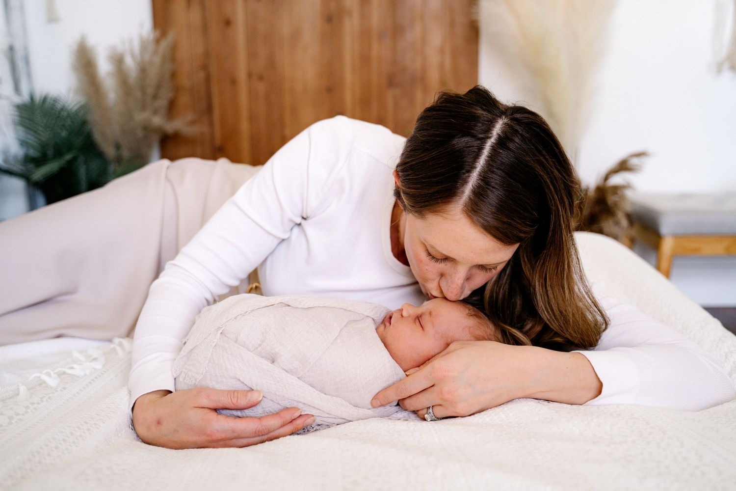 A tender moment between parent and newborn on a white bed in natural light.