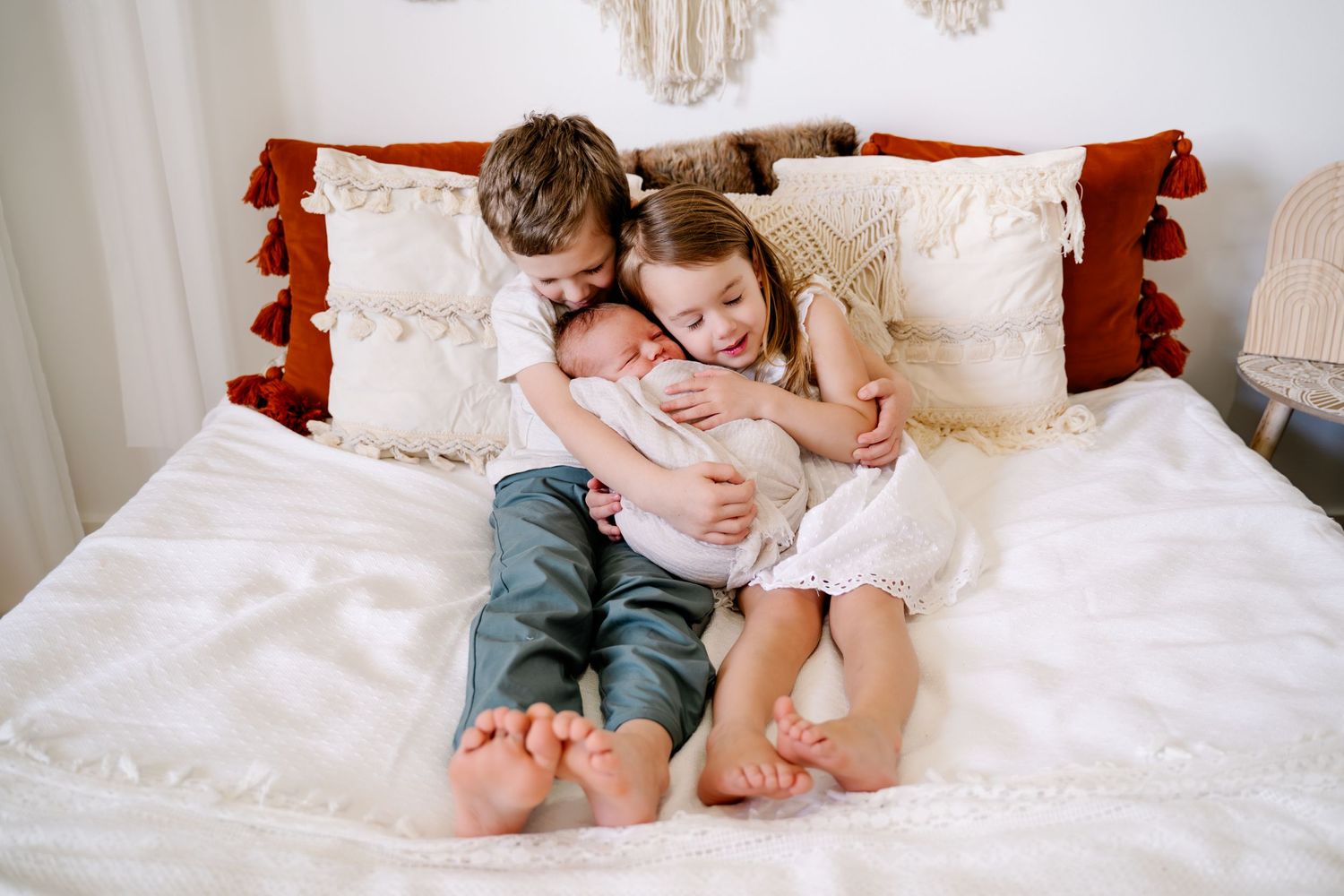 Two children sharing a sweet moment while sitting on a white bed with decorative pillows.