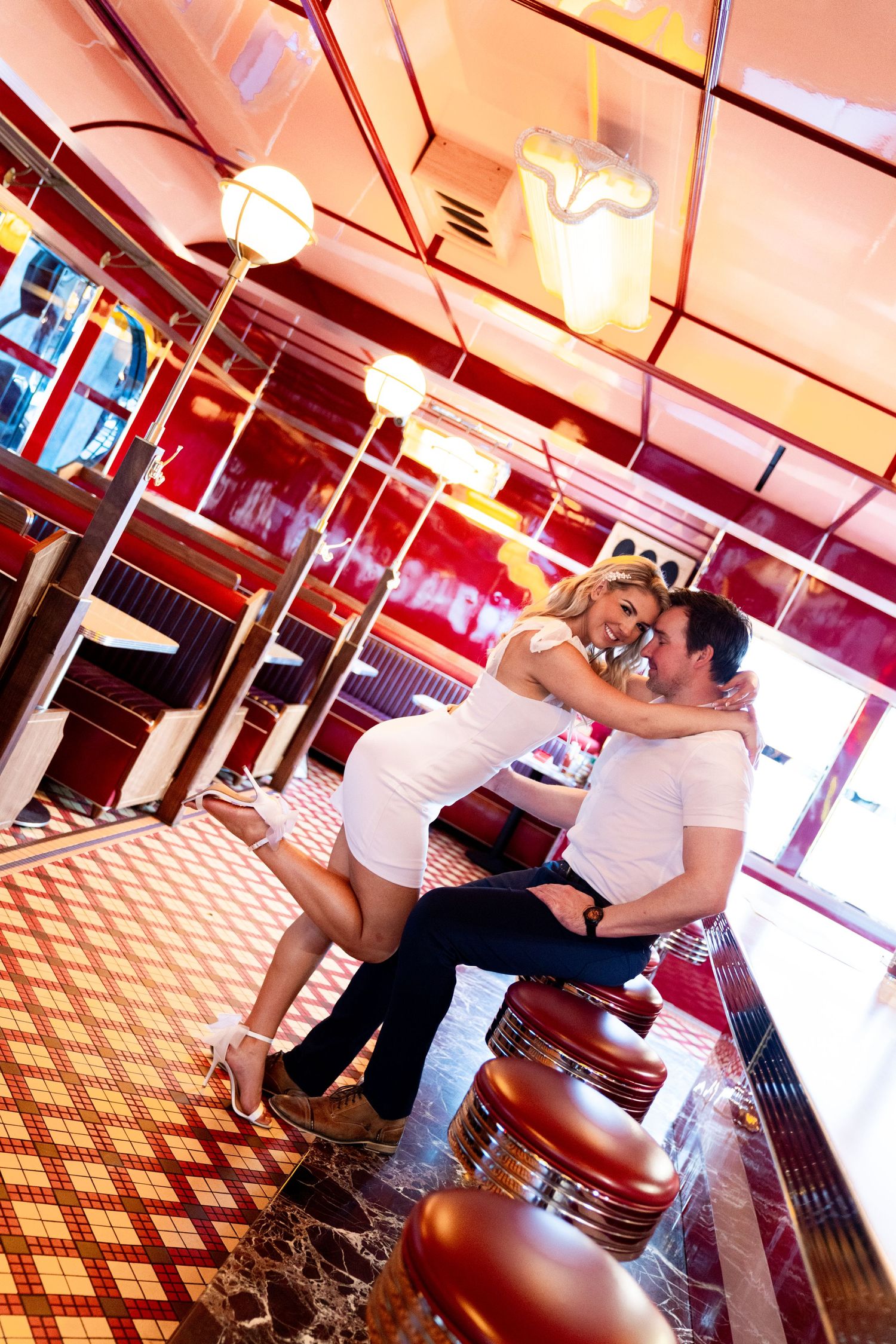 Couple sharing a romantic moment at a retro diner counter with red and white checkered floors. Jessica Paige Photo Co. Best Wedding Photos.