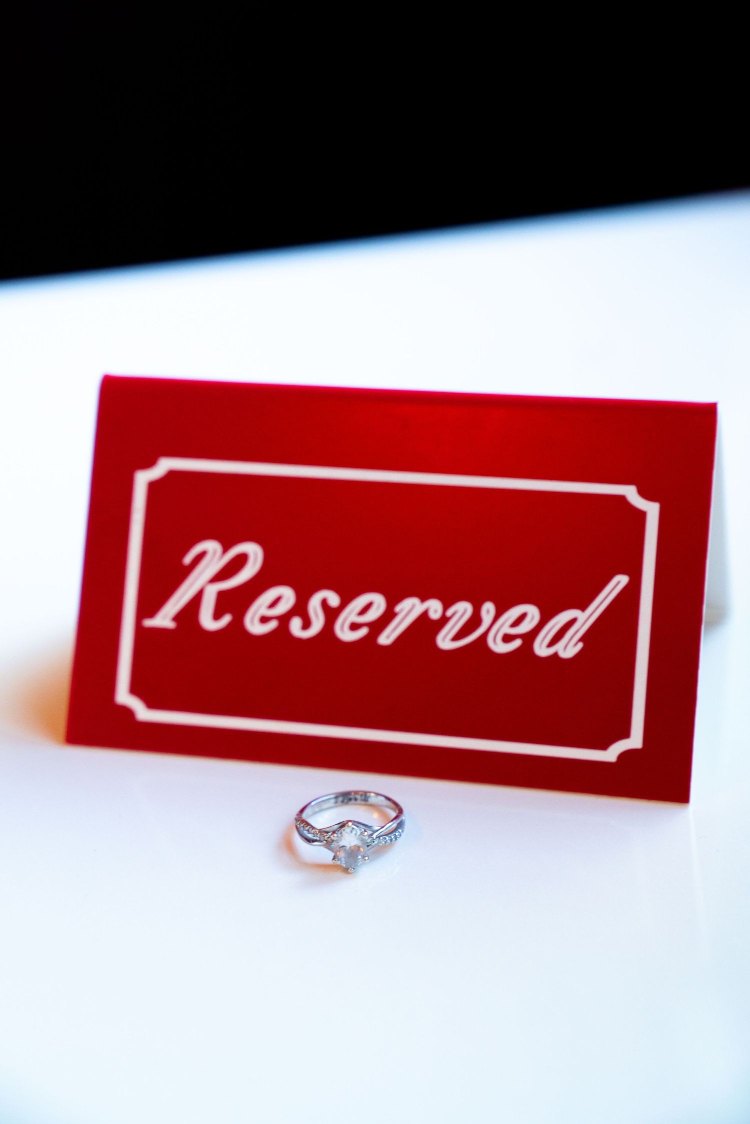 Red reserved sign with diamond engagement ring displayed on white surface. Engagement session at the Lafayette.