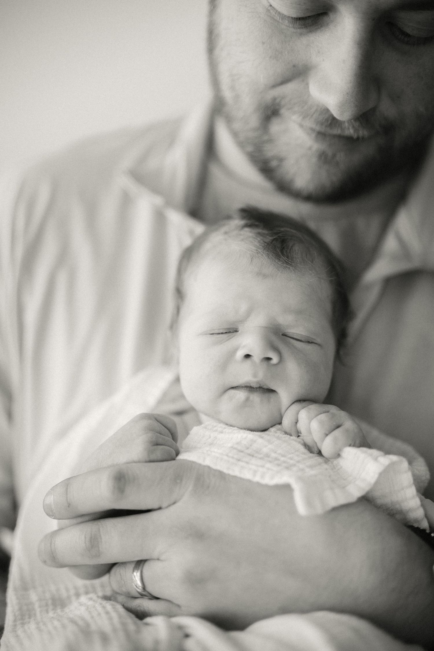 A tender black and white portrait of parent holding a sleeping newborn baby wrapped in light fabric.