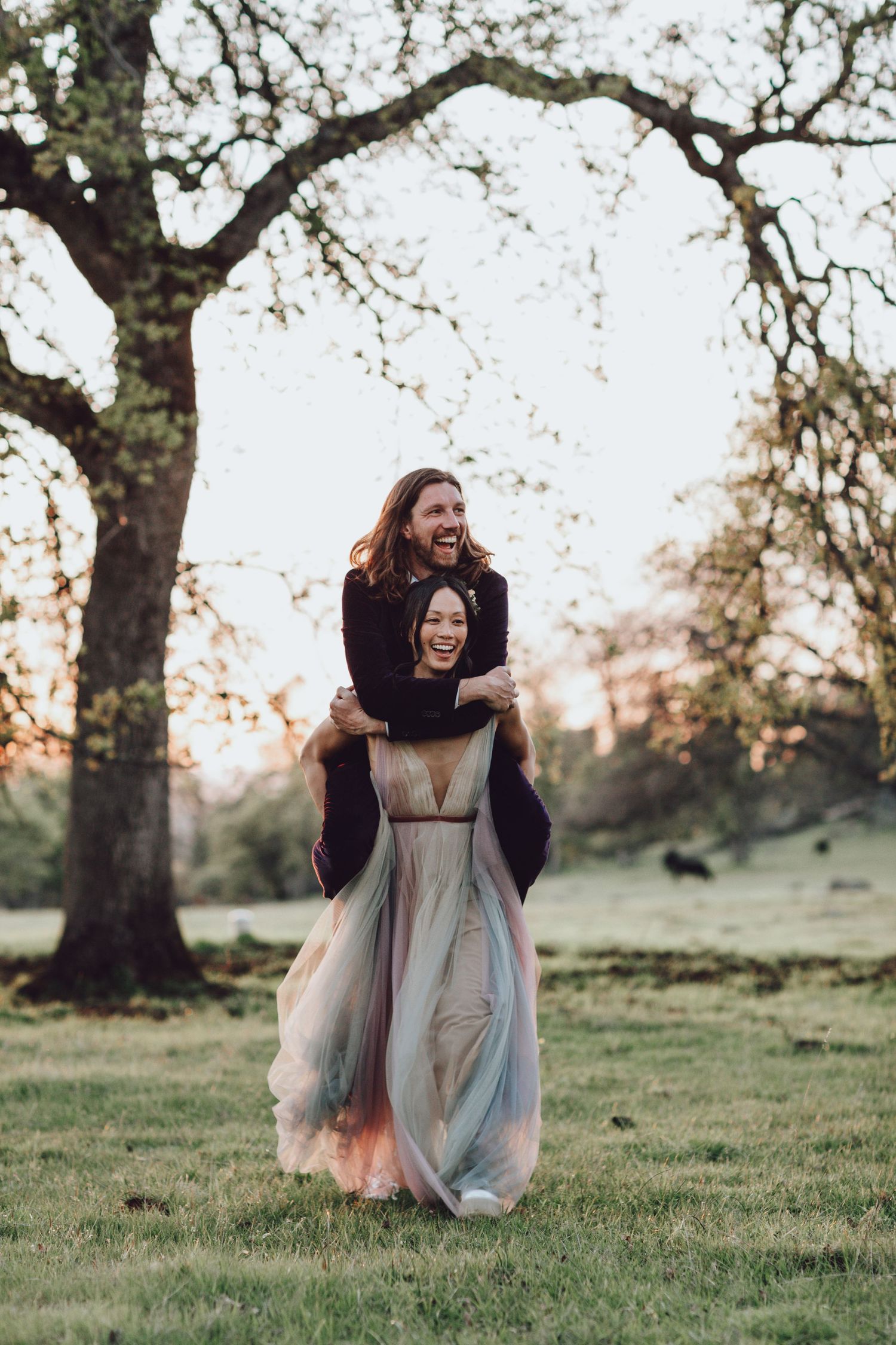 bride and groom having fun in an open field, , wearing a flowing dress, in the Auburn Hills, CA evoking a soft and moody editorial feel.