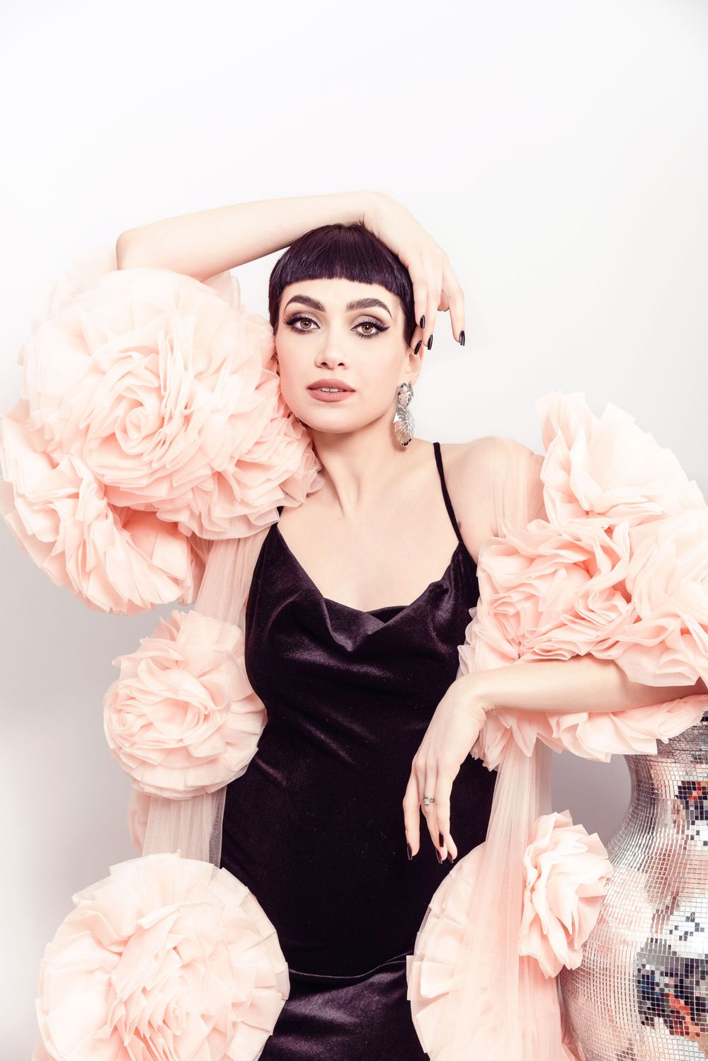 Elegant fashion photo with black silk dress against pink paper flowers and white background.
