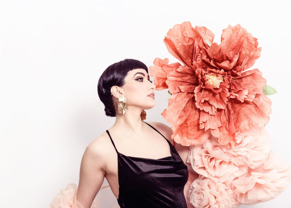 Fashion portrait against white backdrop with large coral pink paper flowers and black spaghetti strap dress.