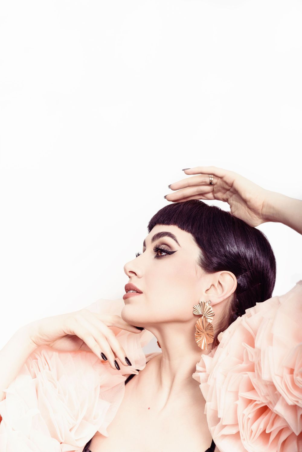 Elegant beauty shot featuring dark hair, dramatic winged eyeliner, and delicate peach floral accents against white background.