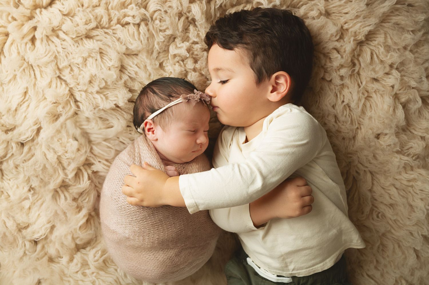 Intimate newborn portrait session with baby resting on cream colored fabric.