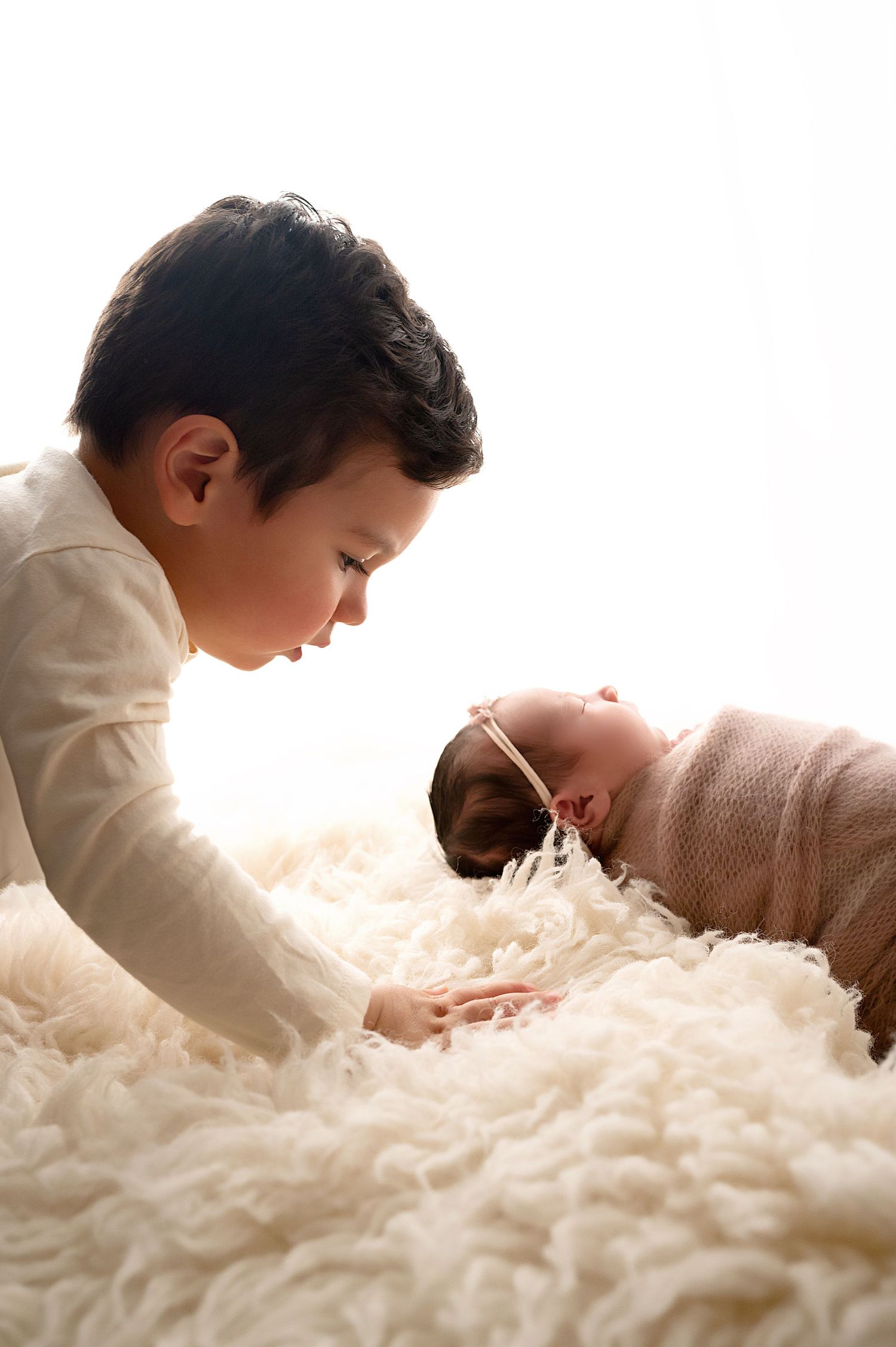 Baby in white lying on soft fluffy fabric while getting photographed.