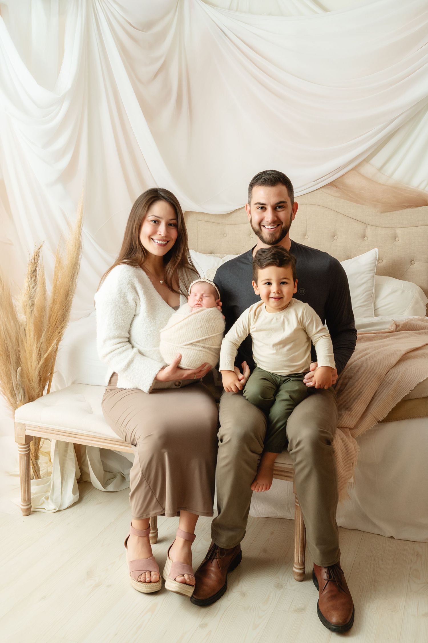 A family sits together on a cream-colored couch with dried pampas grass decor in the background.